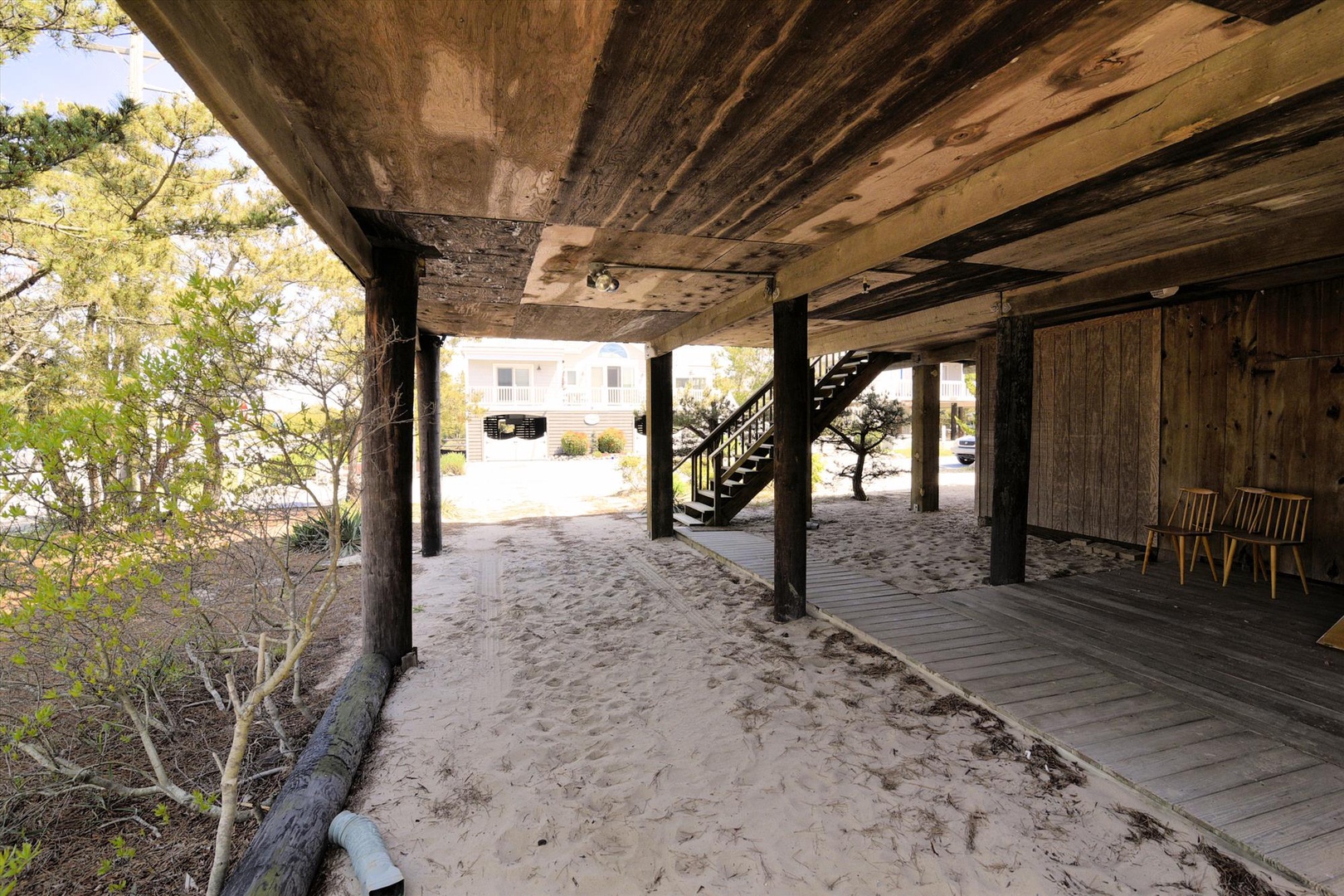 Covered outdoor area beneath the raised property offers sandy ground parking and seating space with coastal charm and direct beach access.
