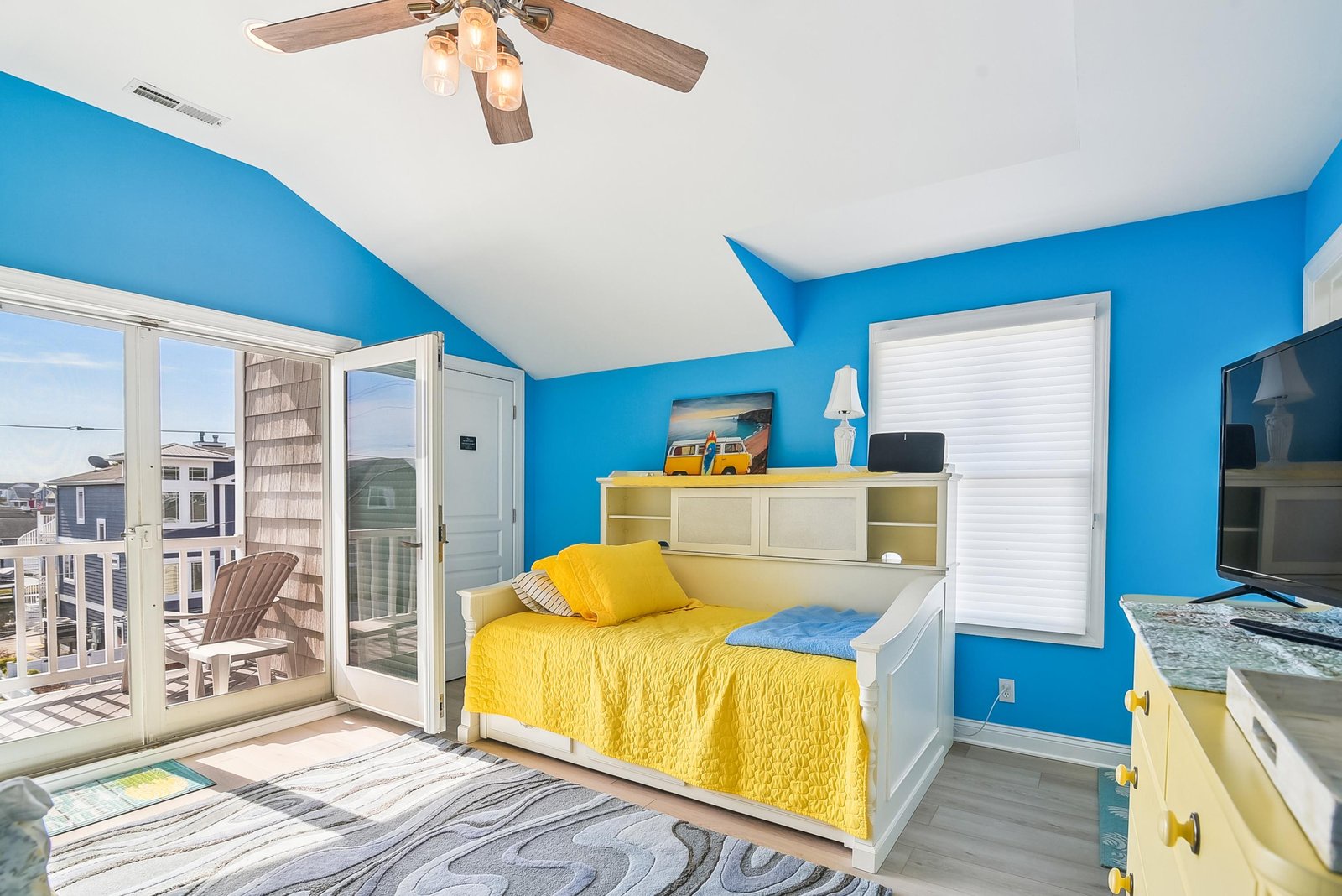 Step into your cheerful coastal retreat with sunny yellow bedding, vibrant blue walls, and balcony doors that invite the sea breeze right in.