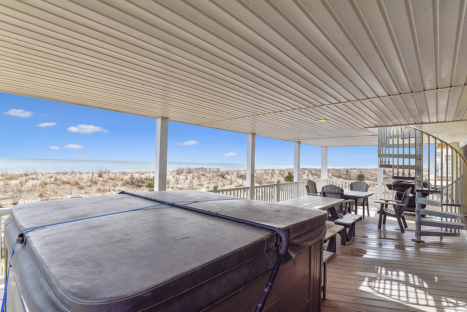 Step onto your private covered deck where a hot tub awaits, perfectly positioned to take in sweeping beach and dune views under the bright coastal sky.