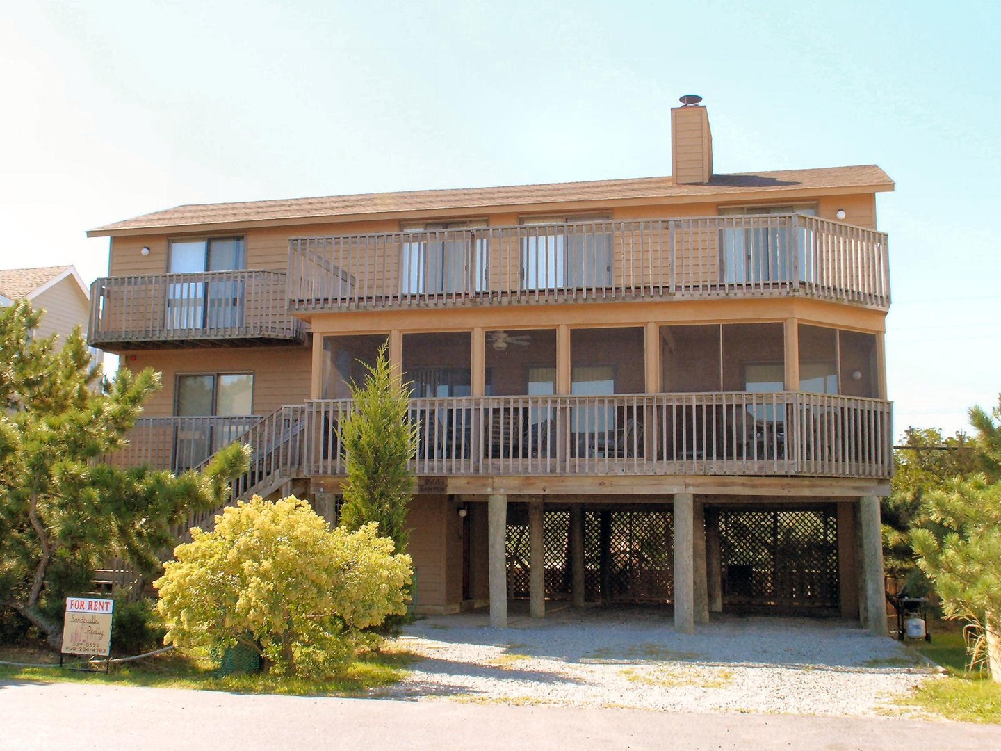 Beachfront property featuring dual waterfront balconies and parking beneath, surrounded by coastal greenery and neighboring homes.