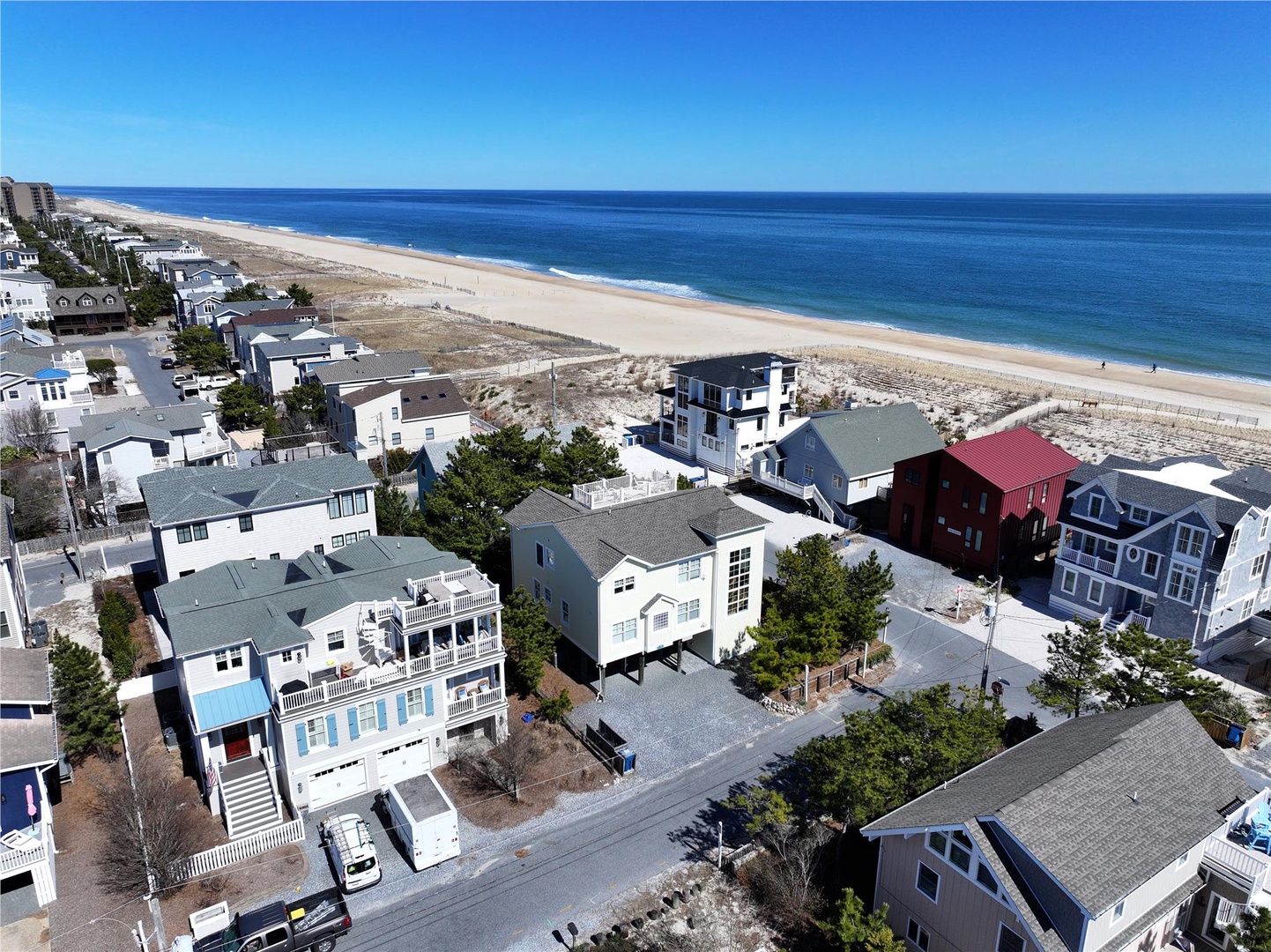 Aerial view of a charming beachfront neighborhood with vacation homes nestled between quiet streets and pristine sandy shores, offering easy access to the sparkling ocean.