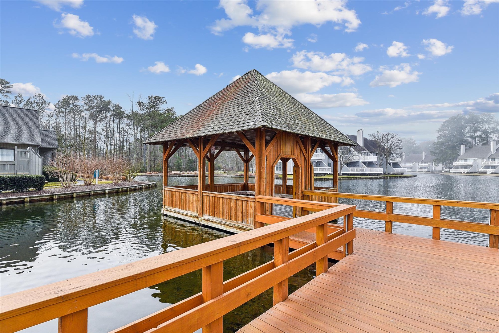 A charming gazebo sits waterfront on a private dock, surrounded by peaceful lake views and the quiet beauty of the community.