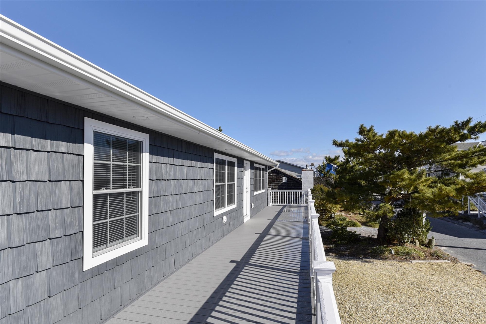 The property features a charming gray shingle exterior with white trim and a spacious deck perfect for your outdoor relaxation. Mature landscaping creates a private, coastal retreat atmosphere.