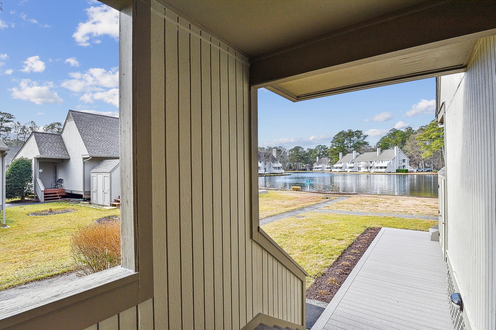 A peaceful lakefront neighborhood setting with nearby homes and green spaces, offering a tranquil residential atmosphere upon arrival.