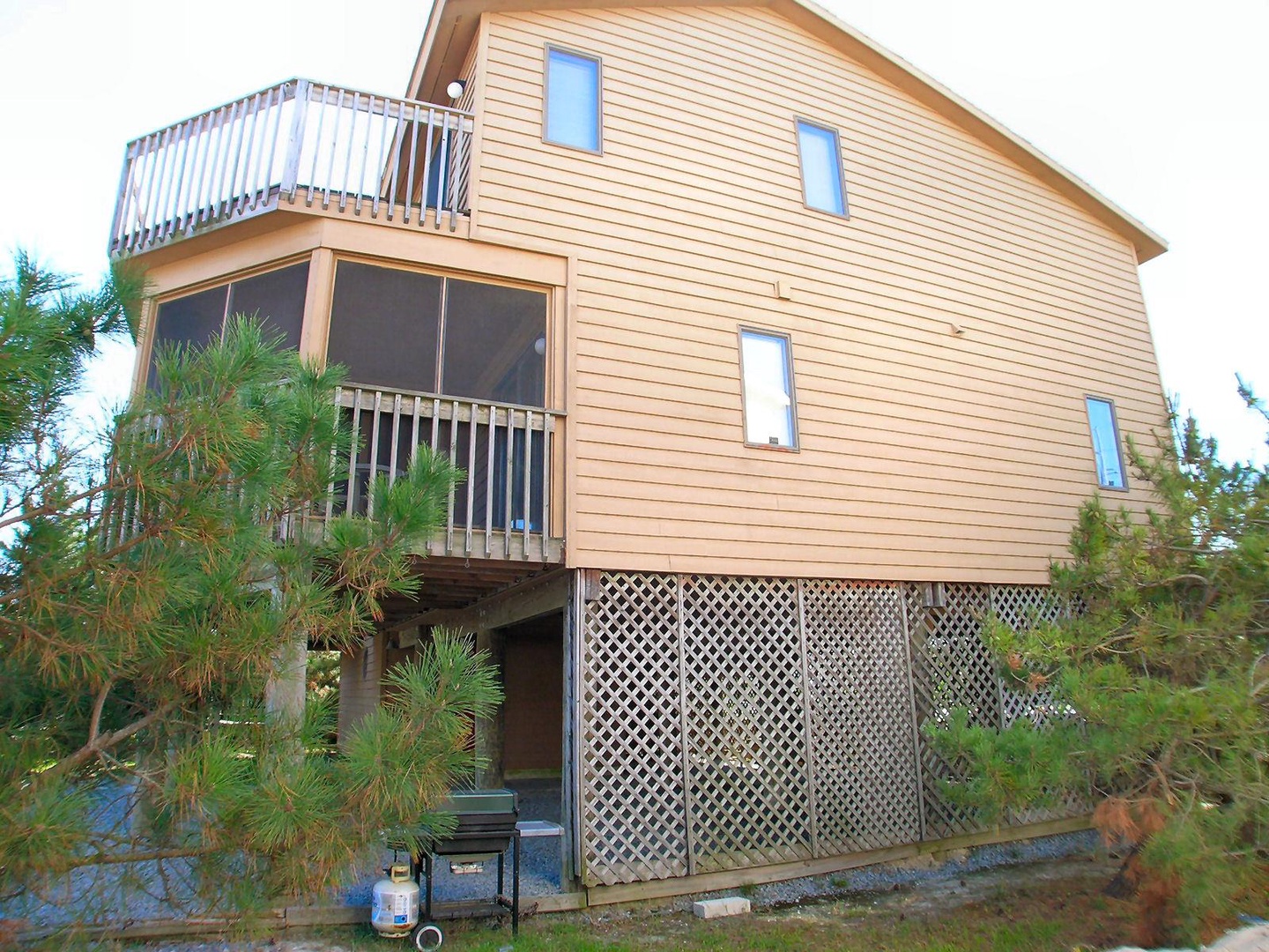 Multi-level coastal retreat with screened porch and open balcony, nestled among native pines near the shore.