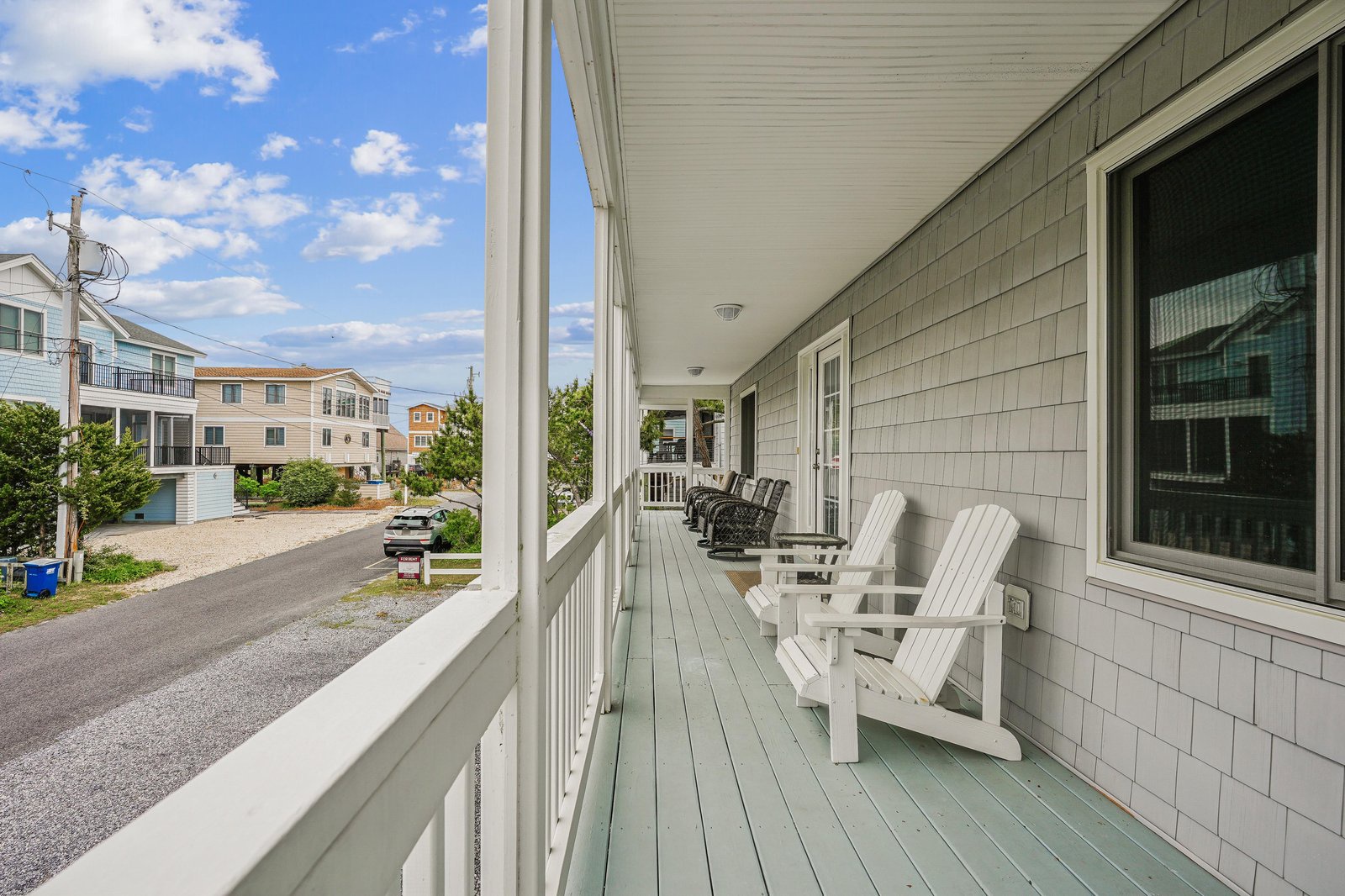 Classic Adirondack chairs line the spacious covered porch, offering a peaceful spot to relax and soak in the coastal neighborhood vibe between beach adventures.