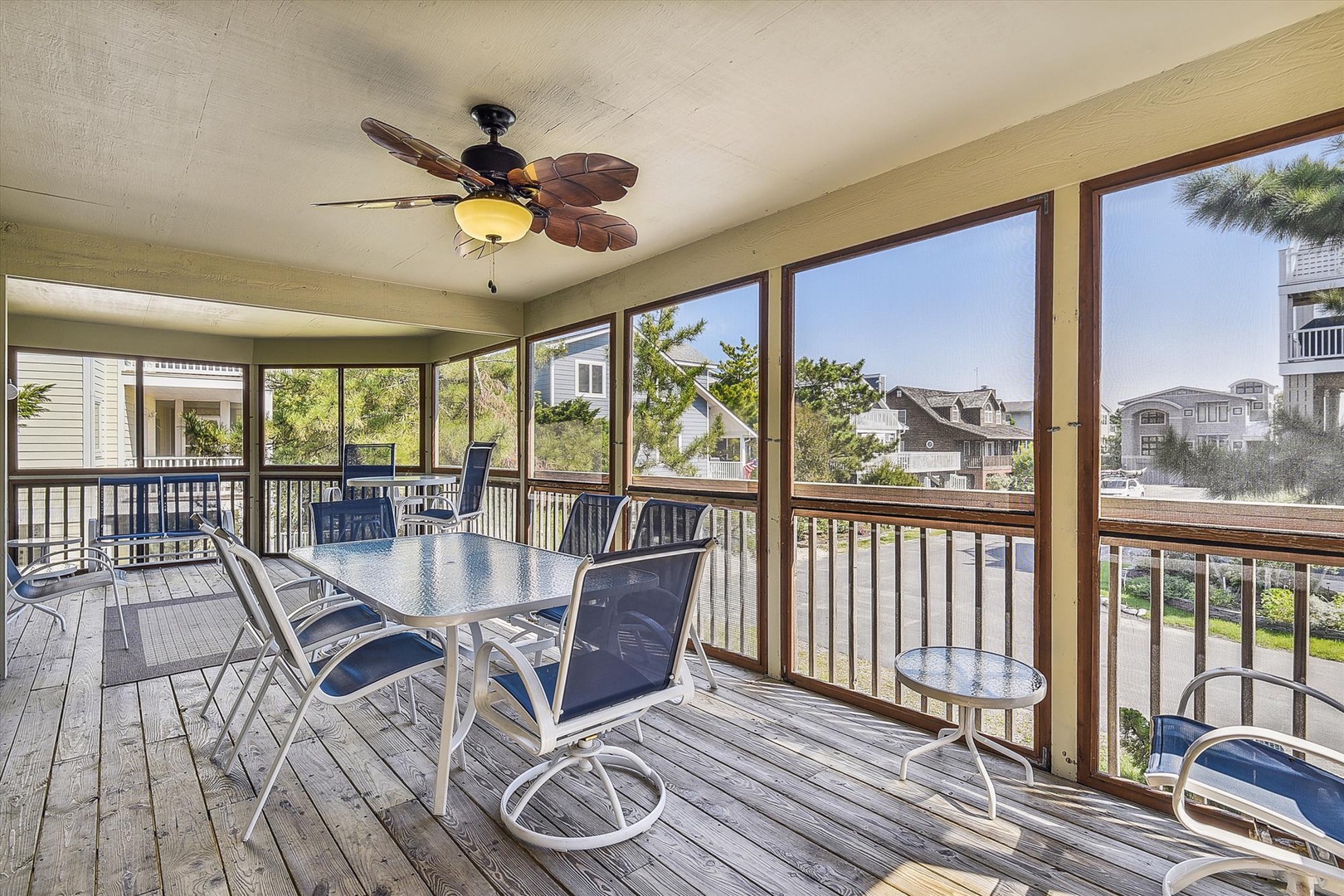 Your screened porch invites relaxation with comfortable dining seating, tropical ceiling fan, and peaceful views of the neighborhood's coastal charm—perfect for morning coffee or evening gatherings.