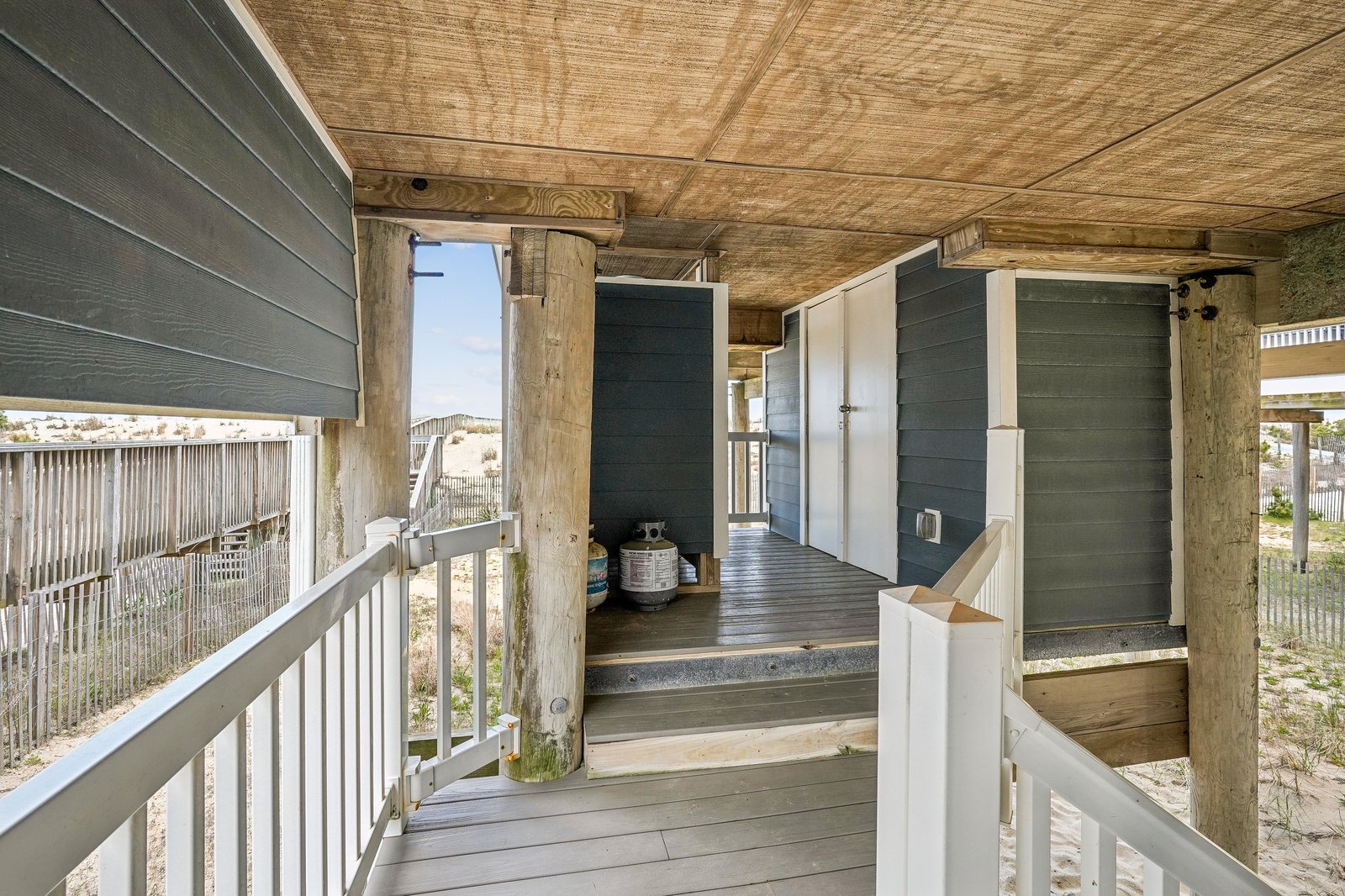 A sheltered porch welcomes you with weathered wood beams and coastal charm, just steps from sandy dunes and open sky.