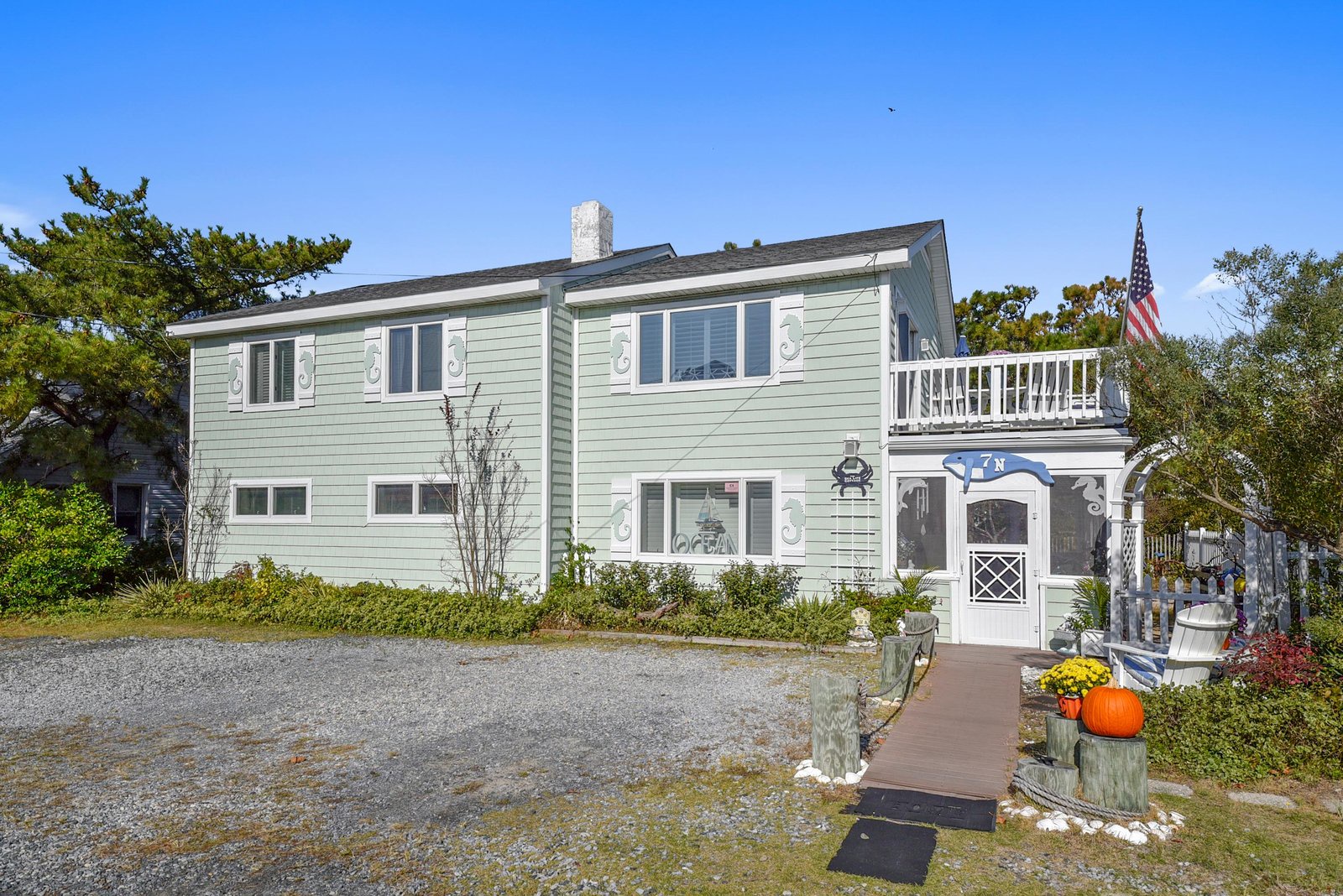 A charming coastal home featuring an upper balcony and welcoming entrance, set among lush greenery and seasonal decorations near the property's entrance.