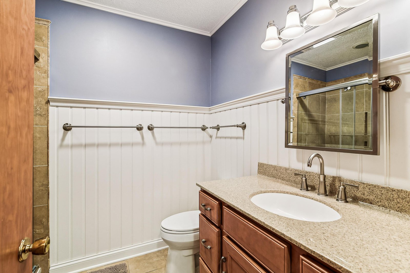 Refresh in your private bathroom with soft blue walls, classic white paneling, and a granite-topped vanity. The warm wood tones and thoughtful lighting create a calming retreat after your day.