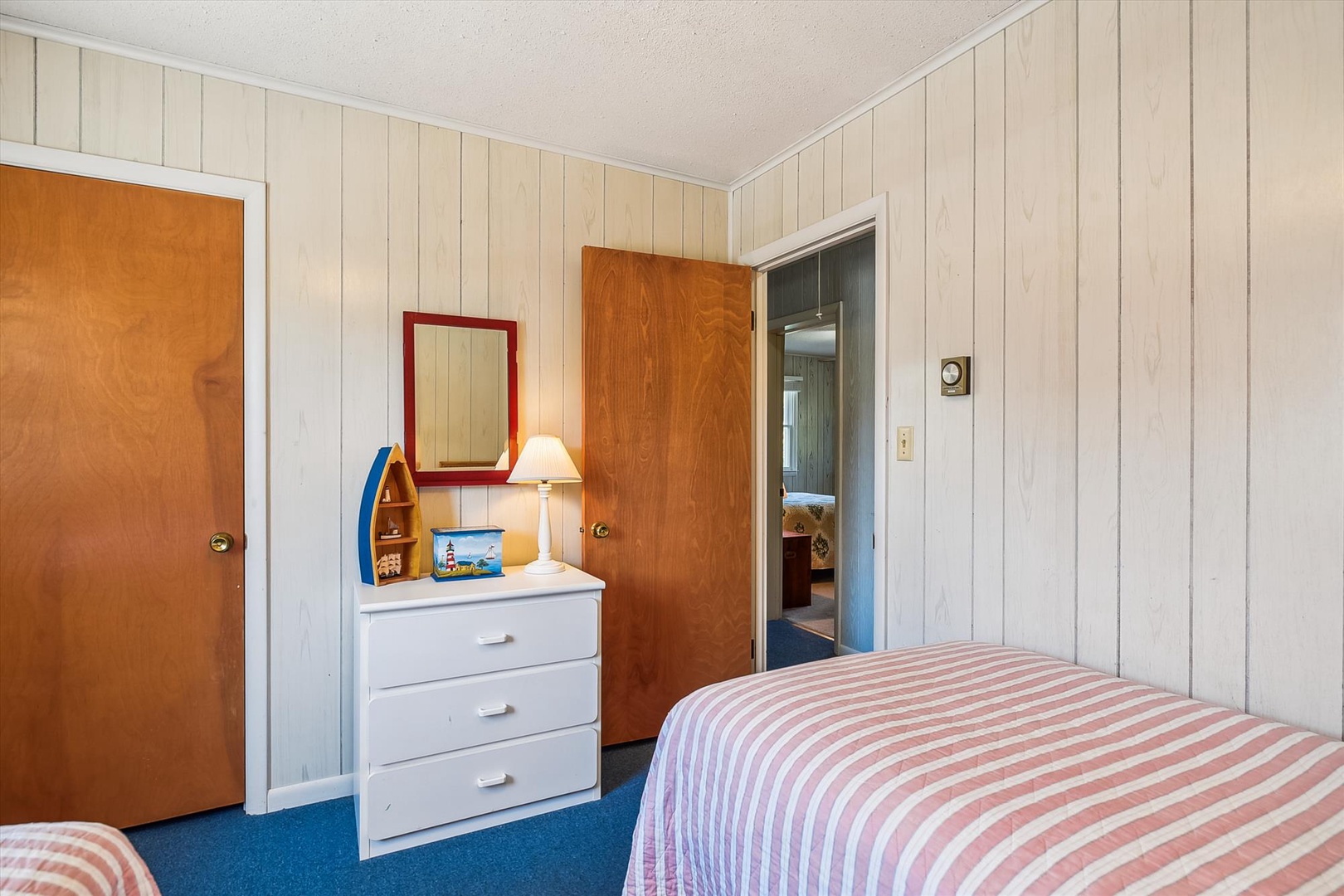 Your cozy bedroom features twin beds with cheerful striped linens, a handy dresser with thoughtful beach touches, and easy access to the adjoining bathroom—perfect for restful mornings.