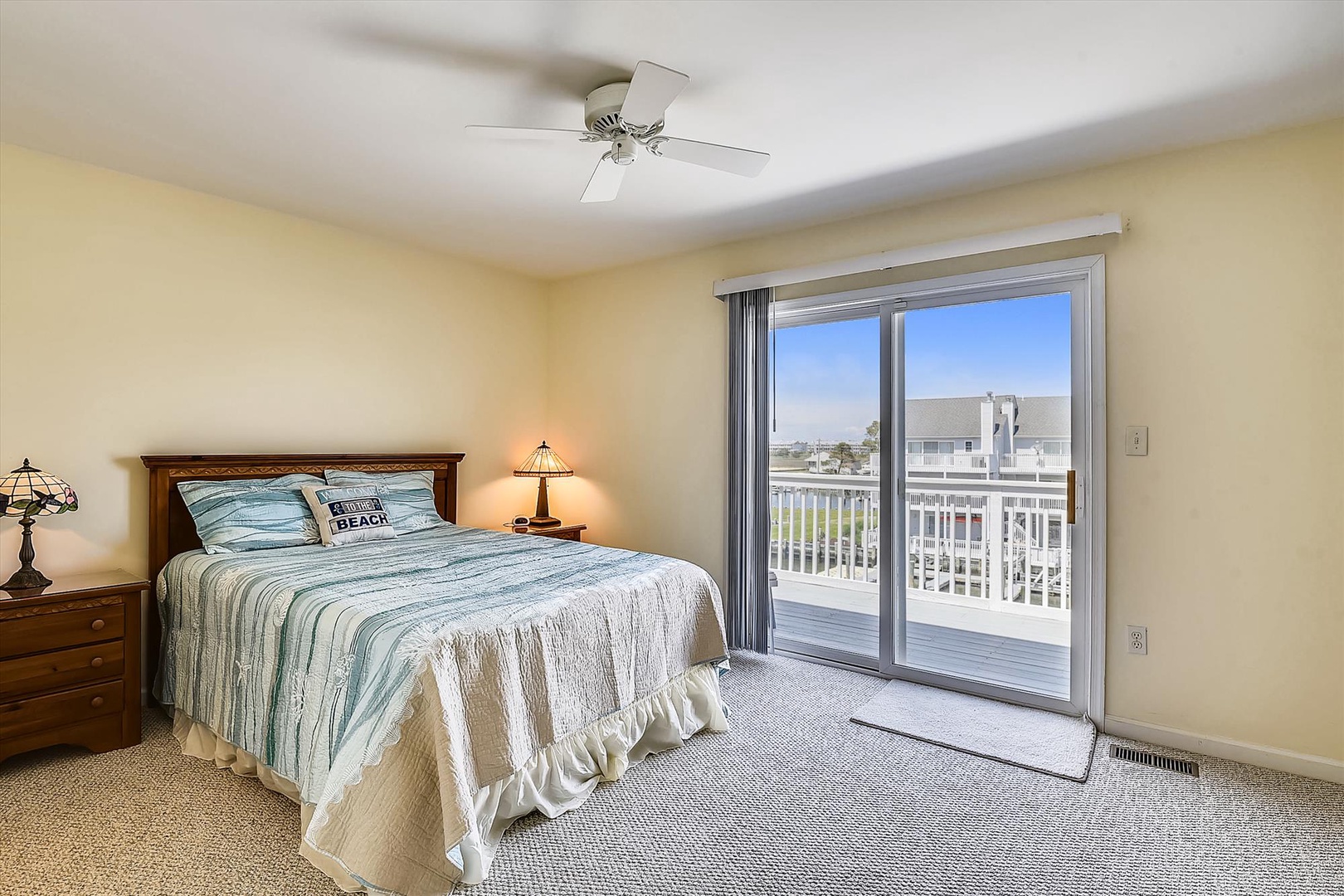 Your serene bedroom features a comfortable bed dressed in coastal-inspired linens and opens to your private balcony. Wake up to gentle breezes from the ceiling fan and natural light streaming through the sliding glass doors.