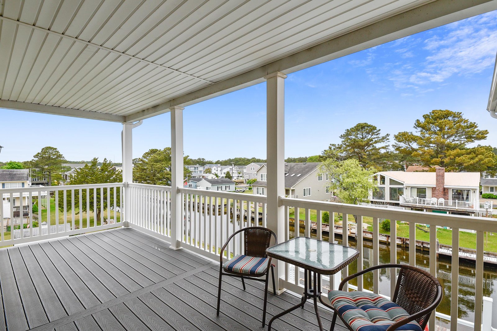 A covered balcony overlooks a peaceful waterfront neighborhood, with comfortable seating perfect for your morning coffee or evening unwind.