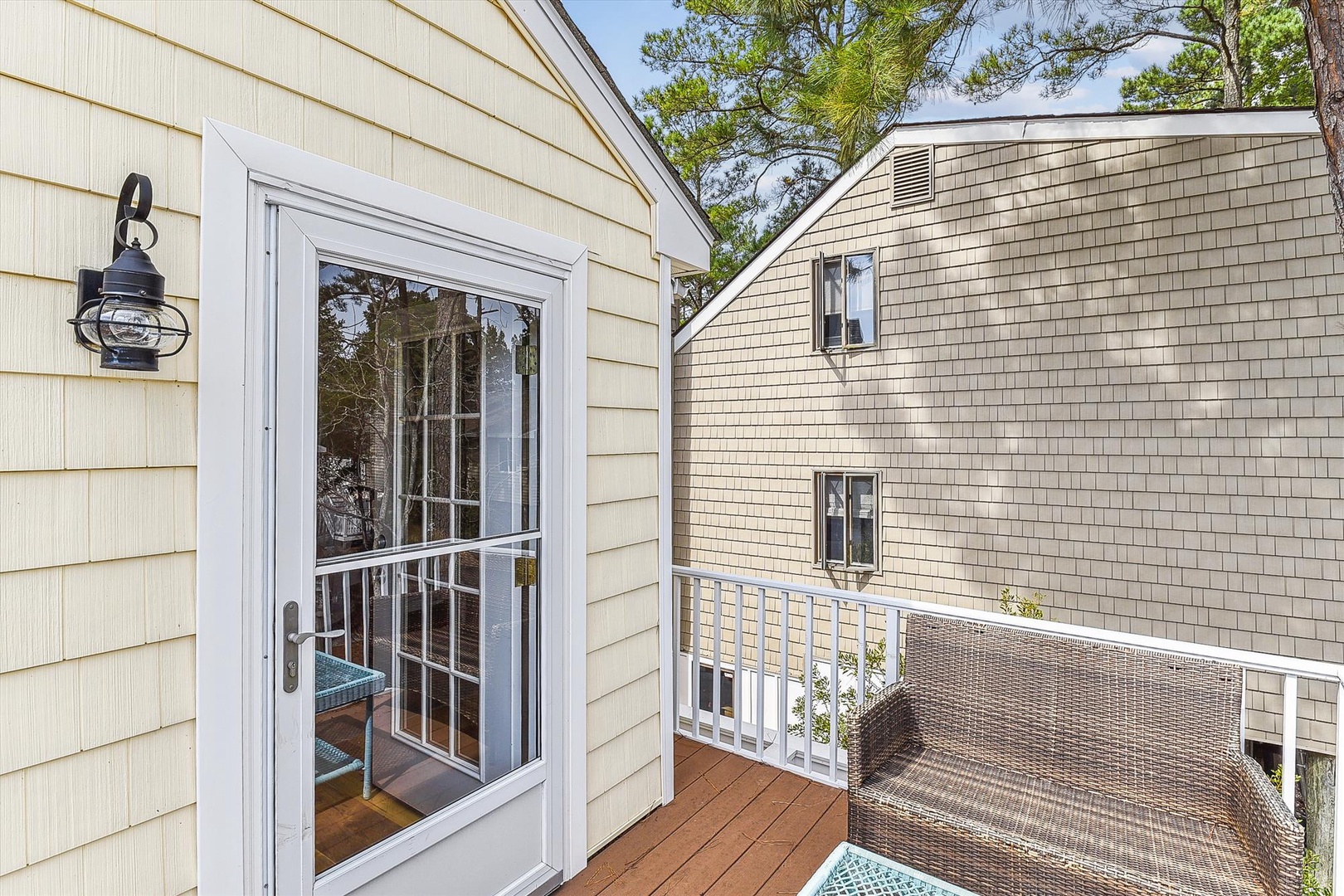 A property featuring light-toned siding and natural landscaping, photographed during the day under clear blue skies with mature trees in the background.