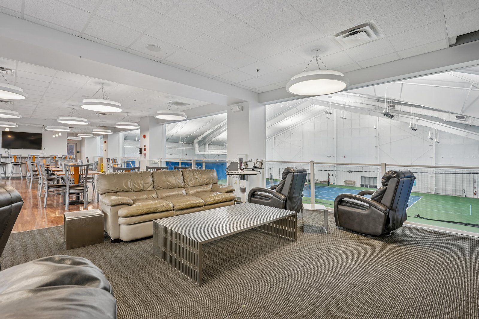Spacious communal lounge with comfortable seating overlooks indoor sports courts, offering a welcoming space to relax, socialize, or enjoy a game with fellow guests.