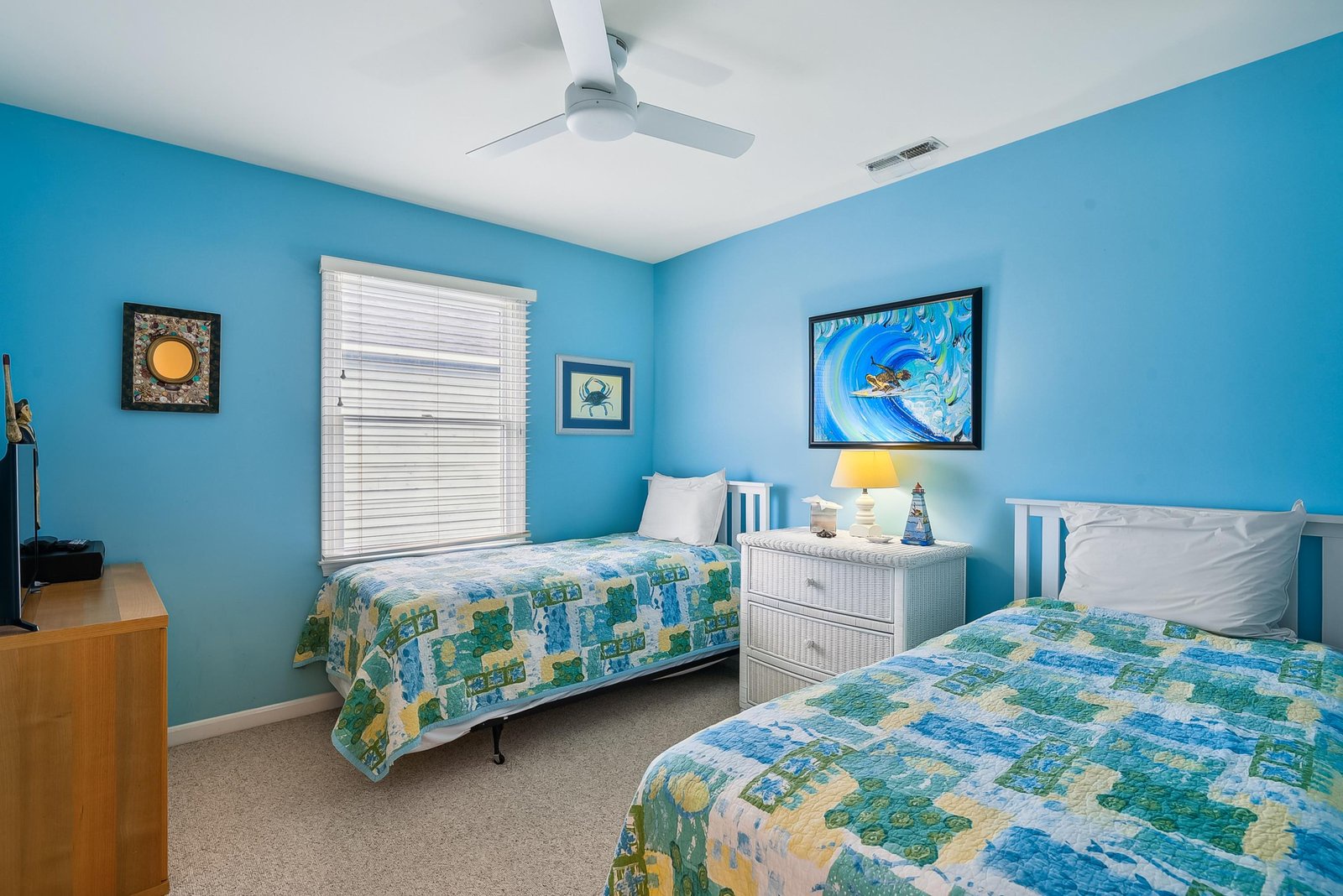 Drift off in your cheerful coastal bedroom, where two comfortable beds invite you and your travel companion to relax under a gentle ceiling fan and bright, breezy décor.