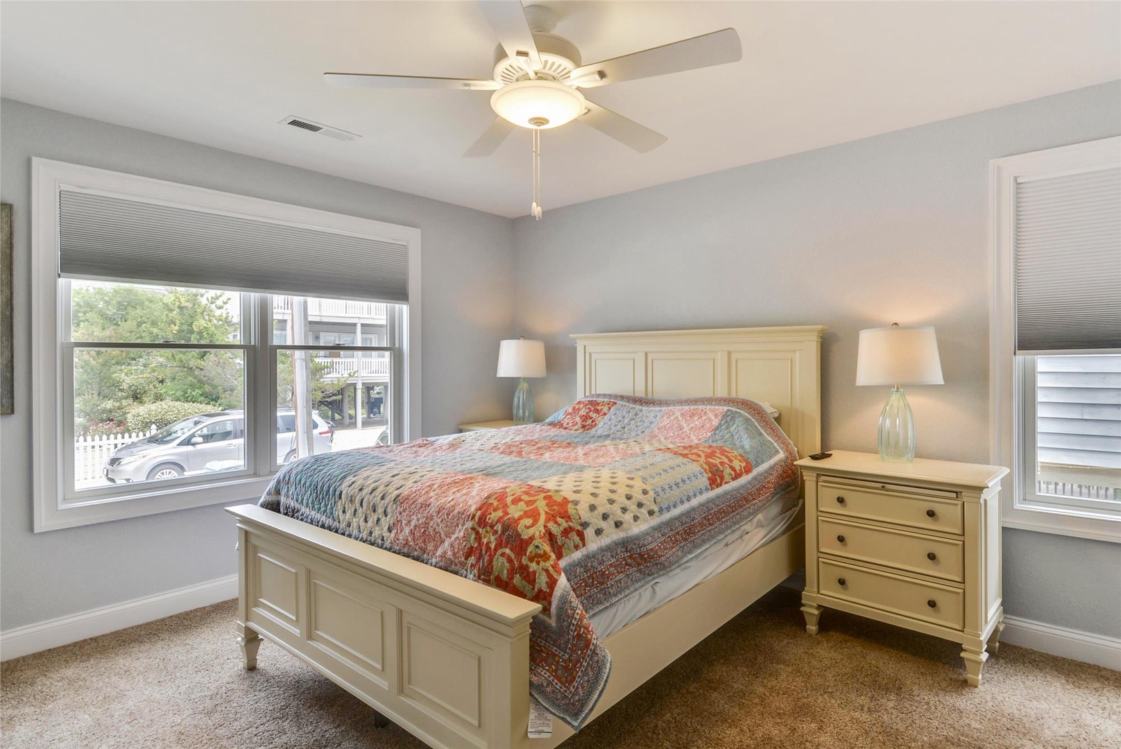 Unwind in your serene bedroom with soft gray walls, cozy bedding, and gentle natural light from two windows. A ceiling fan keeps you comfortable year-round.