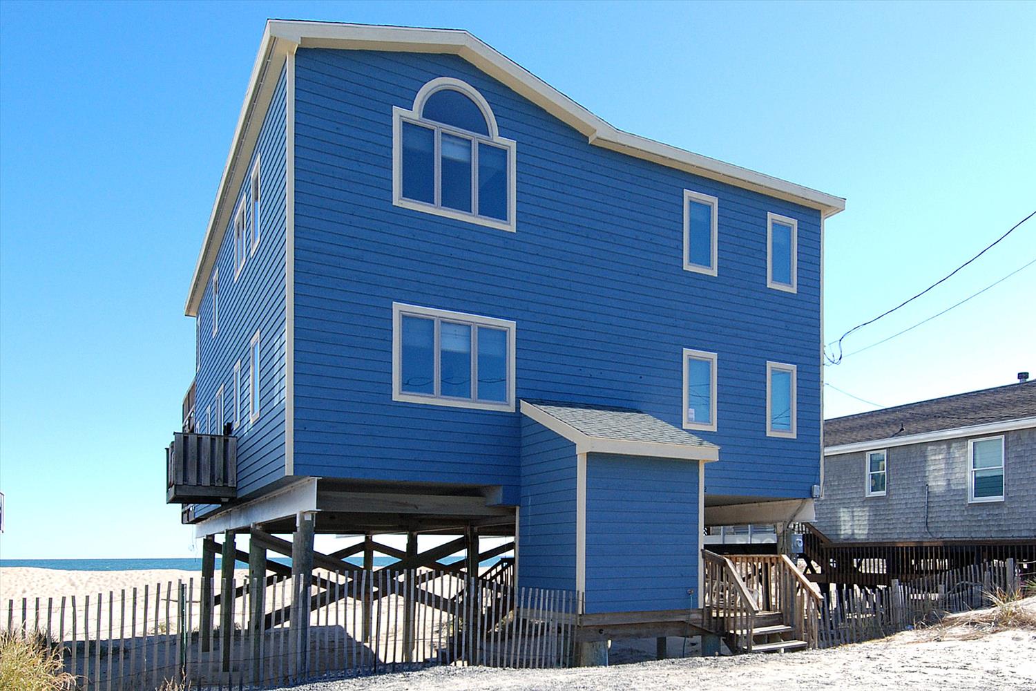 A distinctive blue beach house stands proudly on stilts along the sandy shore. This charming coastal retreat offers direct beach access and stunning oceanfront living.