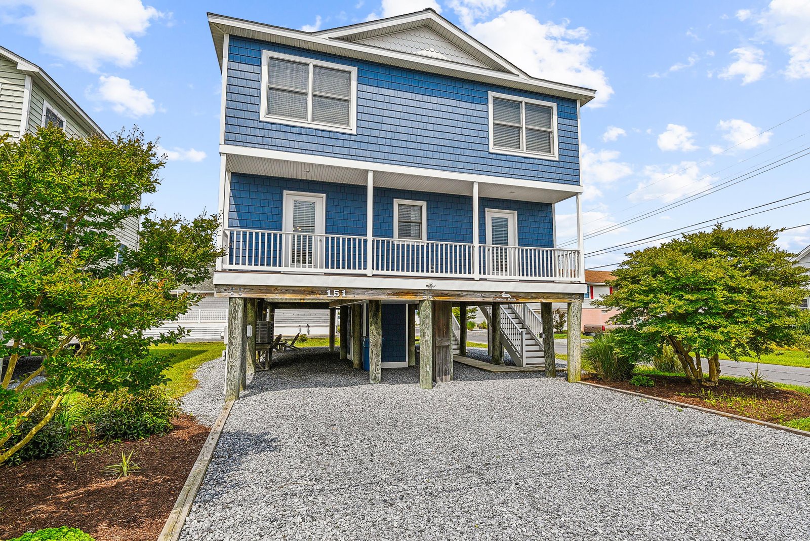 A charming coastal home with distinctive blue siding, welcoming front porch, and convenient ground-level parking awaits your arrival in a peaceful neighborhood setting.