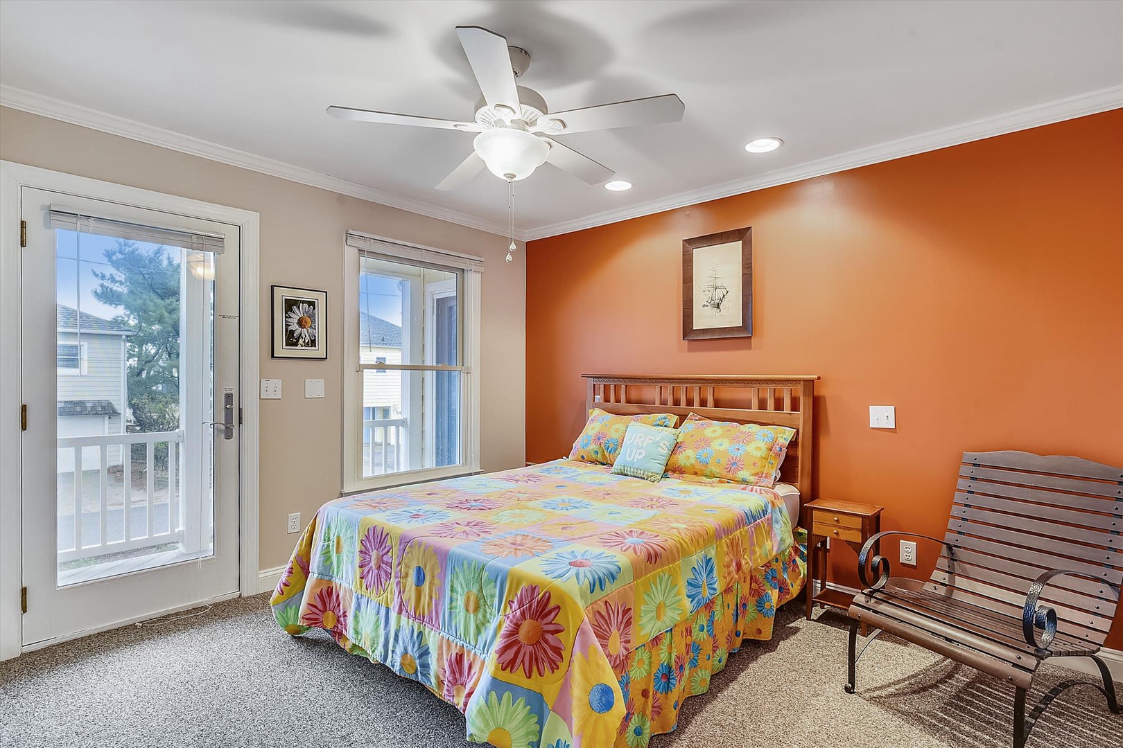Settle into your cheerful bedroom with its vibrant accent wall and ceiling fan, where bright florals and a comfy bed welcome you home after a day of coastal exploration.