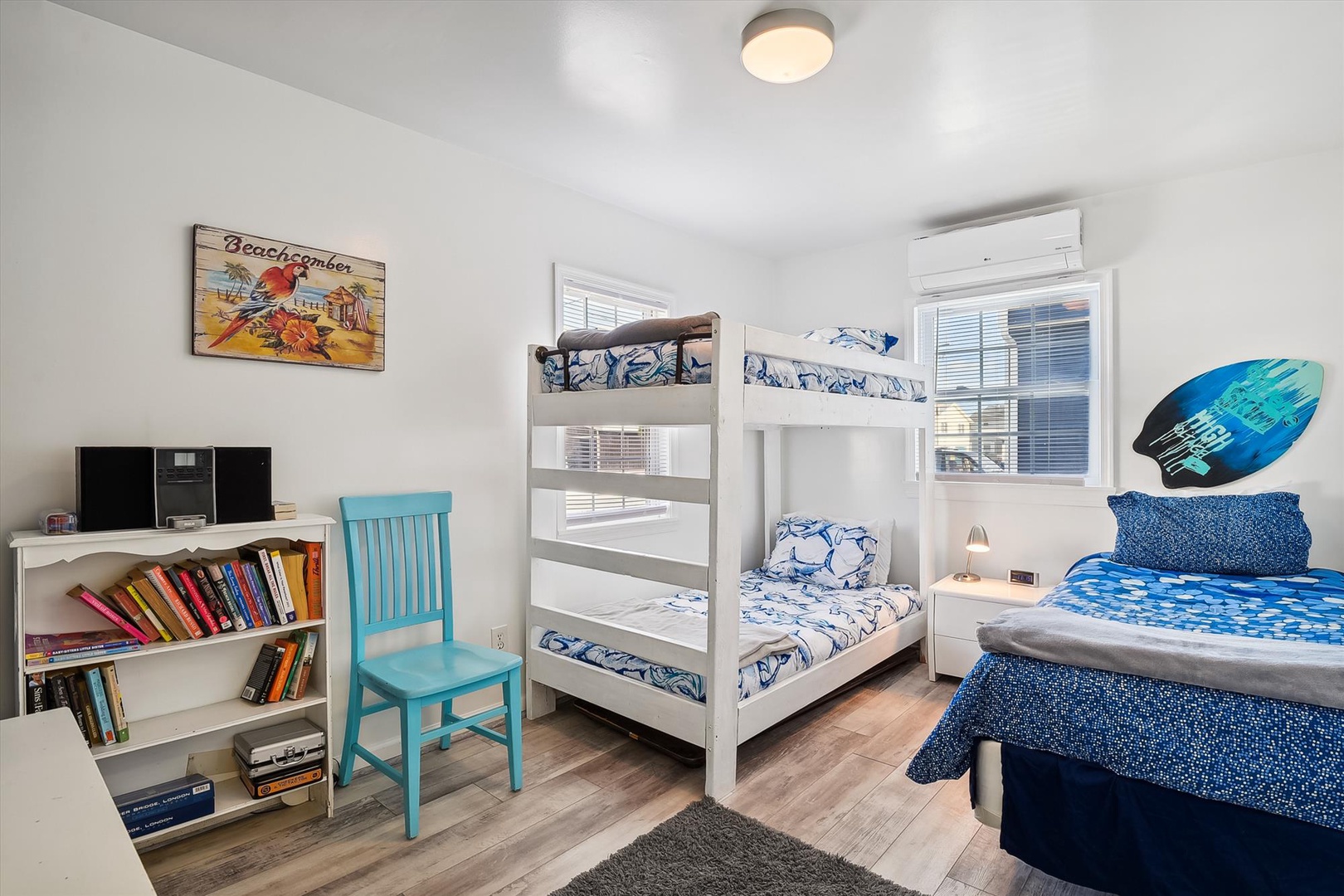 Your comfortable bedroom welcomes with bright, beachy decor—bunk beds for the kids, a cozy single bed for you, and playful surfboard accents that set a relaxed coastal vibe.