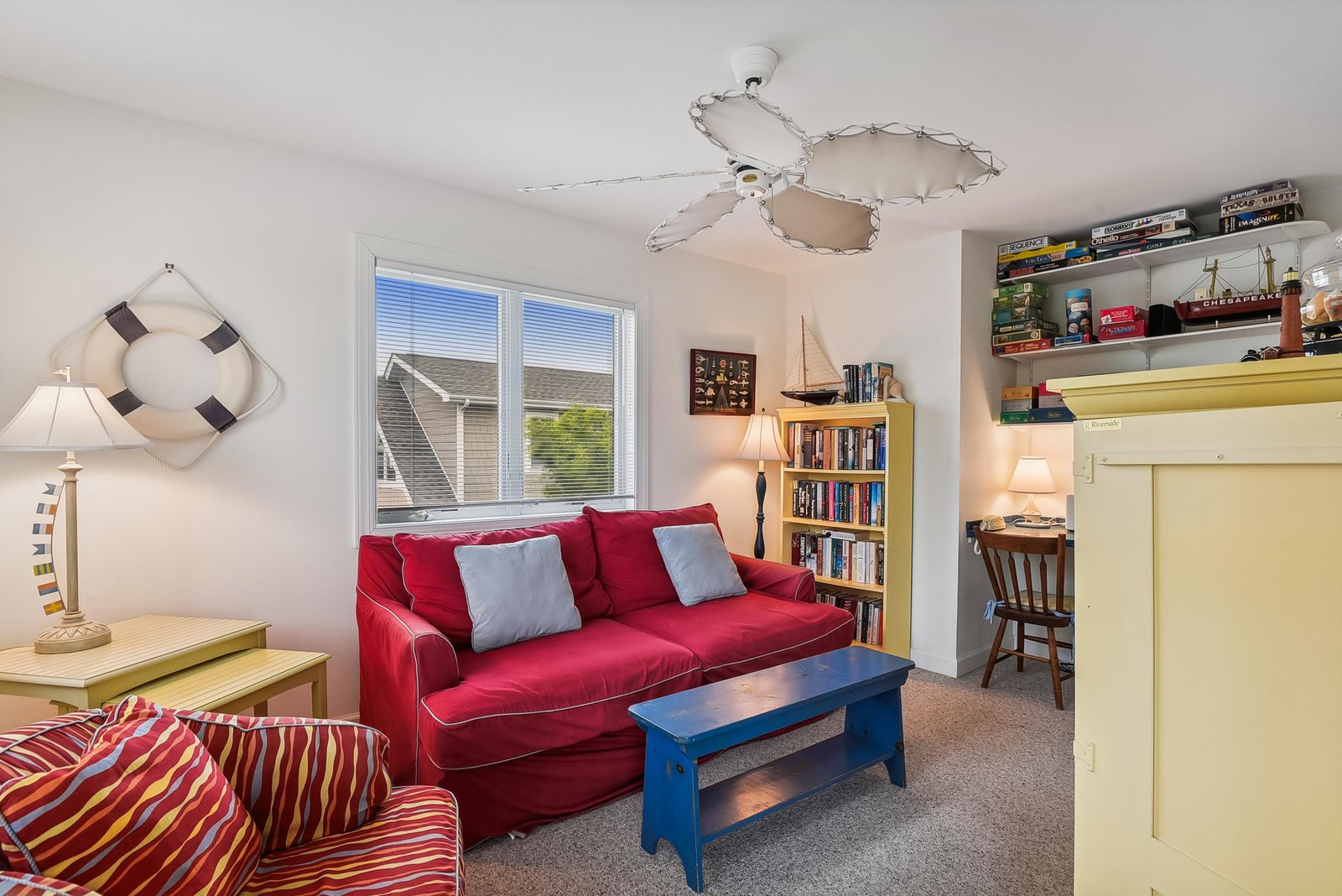 Relax in your cheerful living space with bright red sofa, unique nautical-style ceiling fan, and a cozy reading nook filled with books for your downtime.