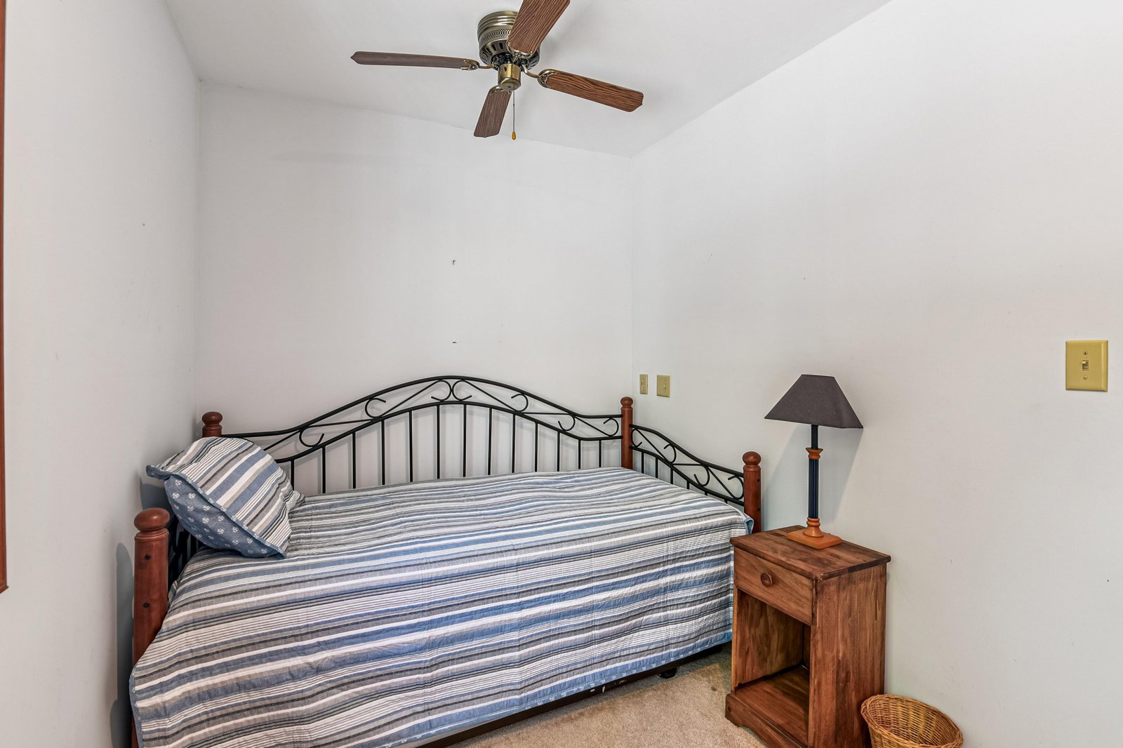 This cozy guest room welcomes you with its simple, clean design—a daybed dressed in classic striped linens, a rustic wooden nightstand, and a ceiling fan overhead to keep you comfortable year-round.
