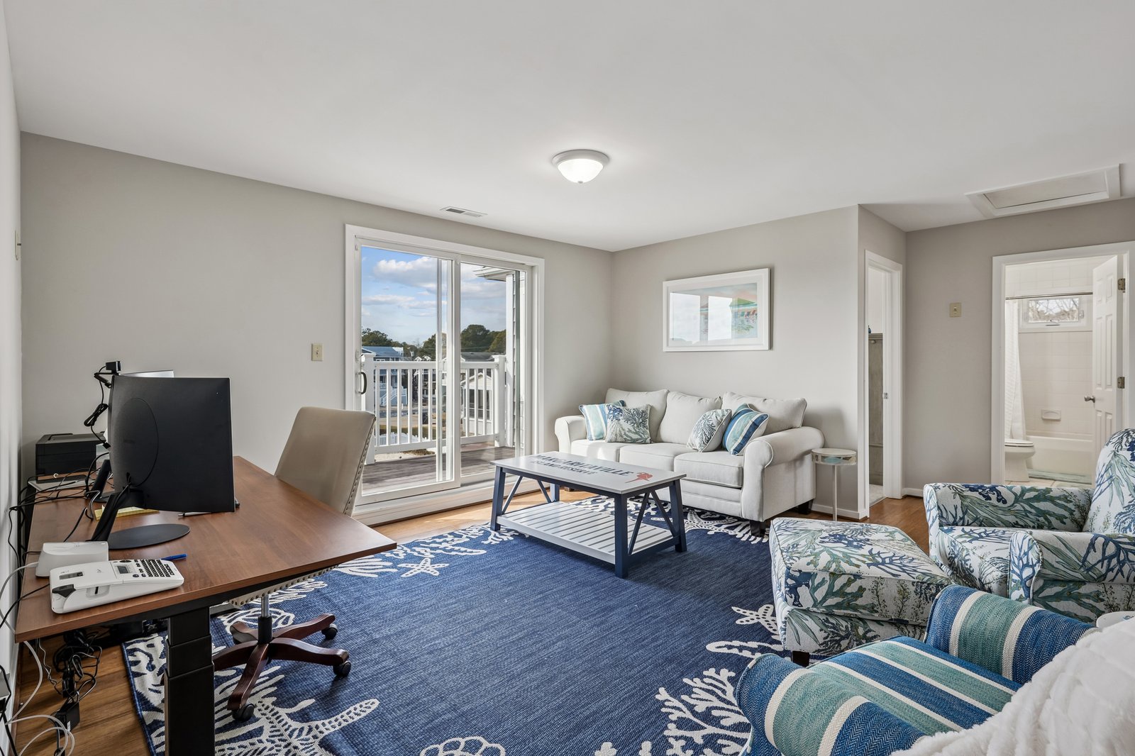 Relax in your bright living room with coastal blues, comfy seating, and balcony access overlooking peaceful neighborhood views.