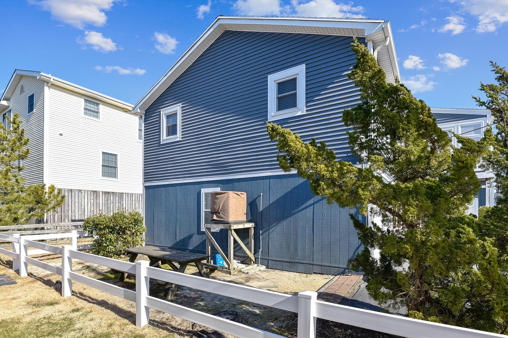 Charming blue coastal home with white trim, surrounded by greenery and neighboring properties in a peaceful seaside community.
