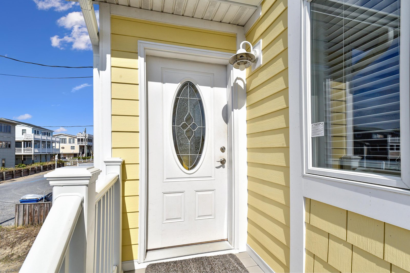 A charming yellow coastal home welcomes you at the front entrance, with bright blue skies and neighboring beach houses creating the perfect seaside getaway atmosphere.