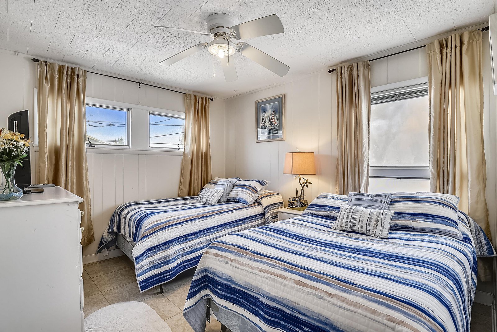 Rest easy in this bright, nautical-inspired bedroom where two comfortable beds await your arrival. The gentle ceiling fan and natural light create a relaxing retreat after a day of adventures.