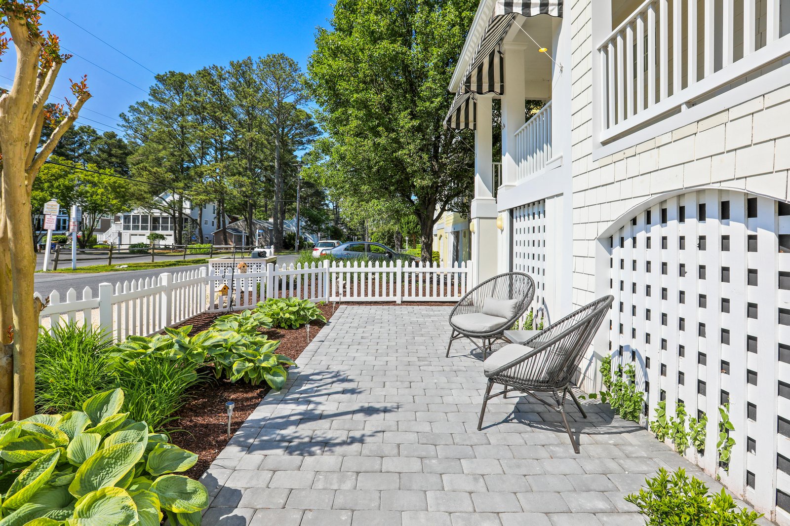 Charming paved patio framed by white picket fencing and fresh landscaping, in a peaceful residential setting.