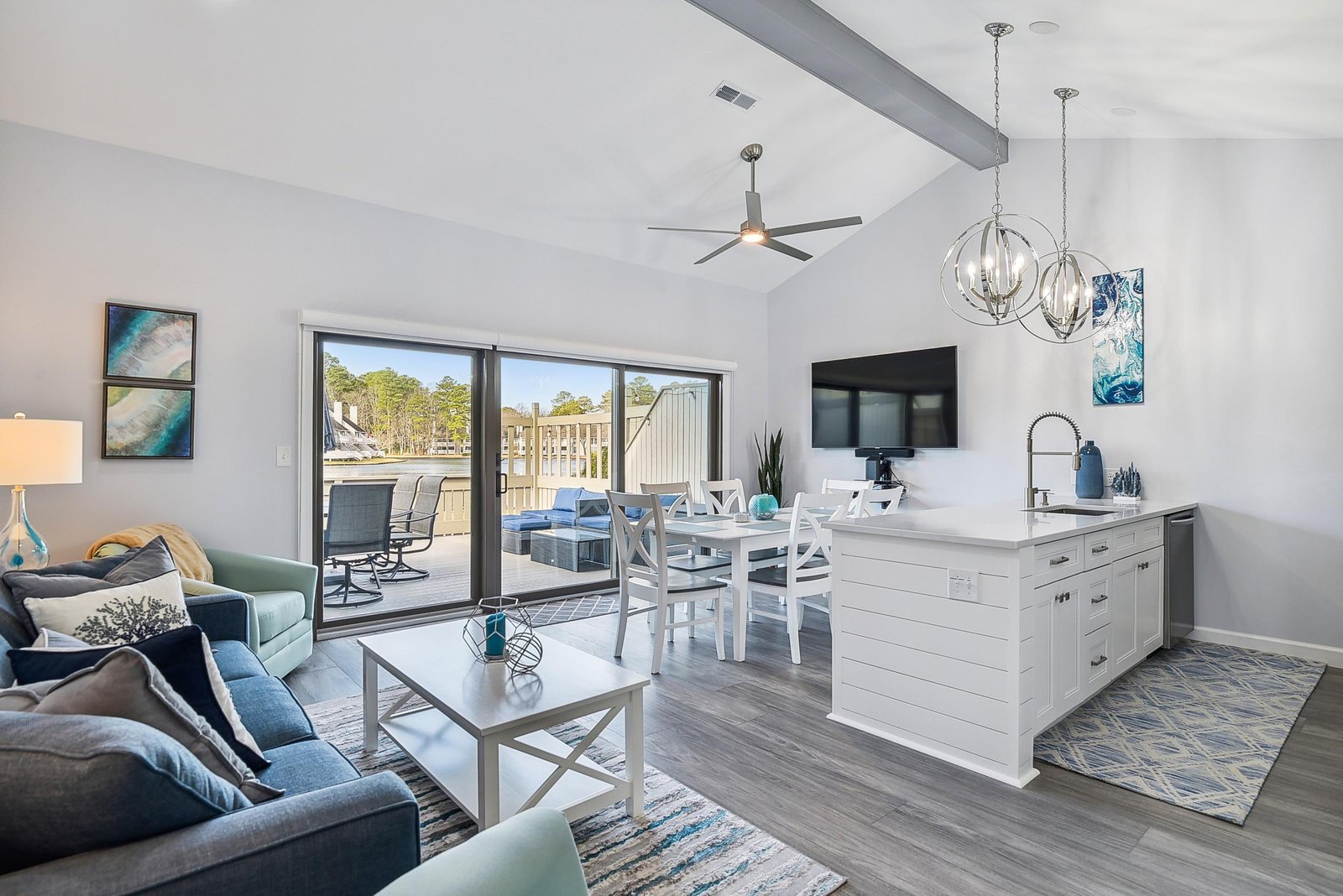 Coastal-inspired open living space flooded with natural light through sliding glass doors, featuring a bright living area, dining table, and kitchen island perfect for gatherings.