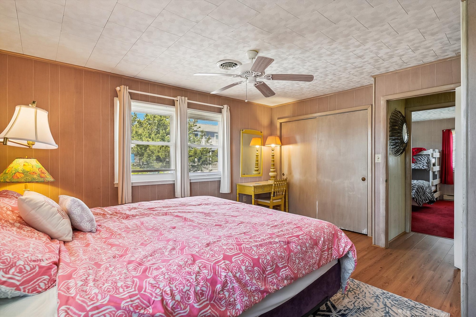 Drift off in a cozy bedroom with soft linens, warm wood tones, and a gentle ceiling fan. Your vanity awaits by the window, with peaceful neighborhood views and a serene retreat vibe.