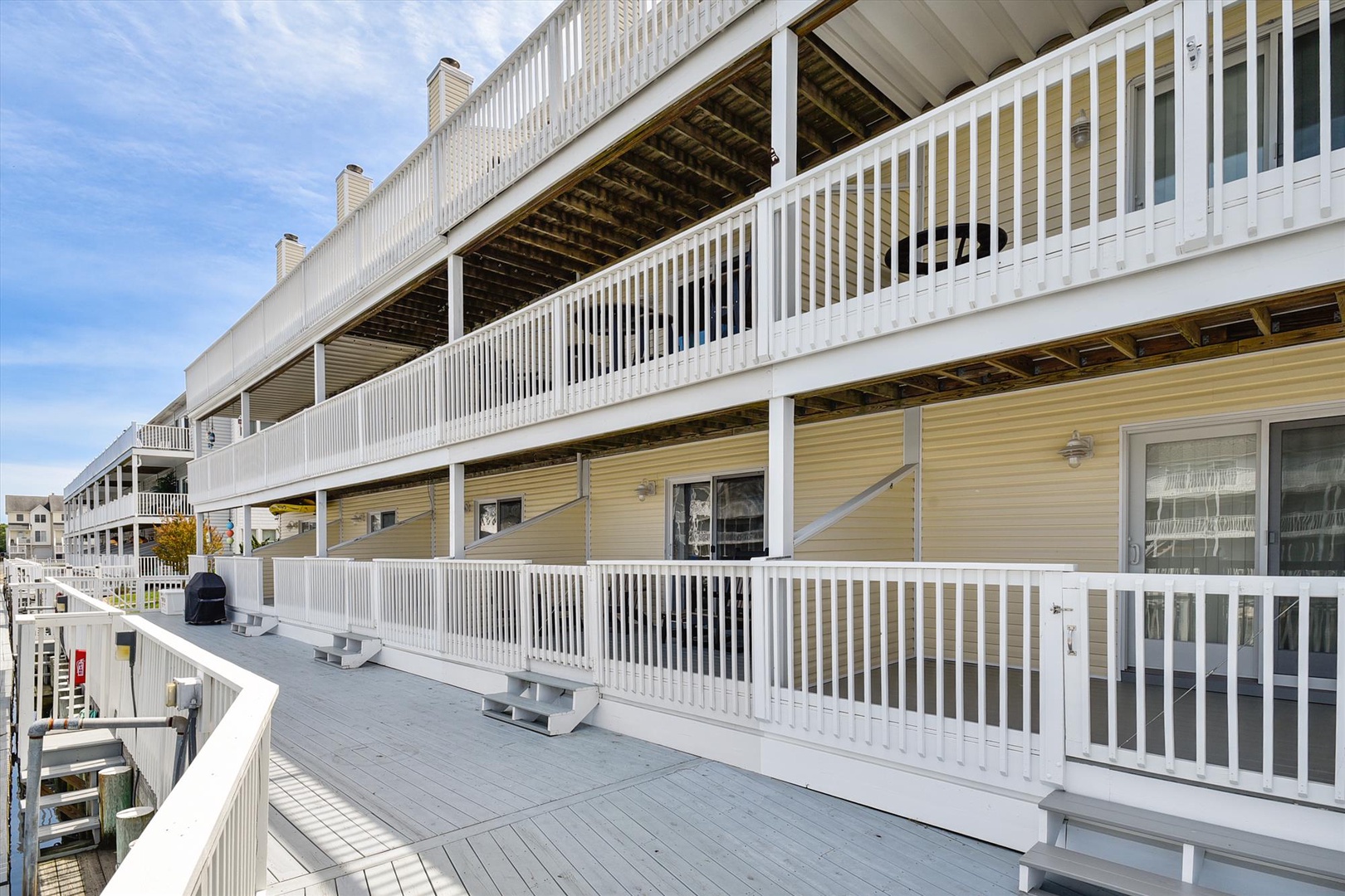 Multi-story building exterior featuring wraparound balconies with white railings, beige siding, and covered walkways overlooking the surrounding neighborhood.