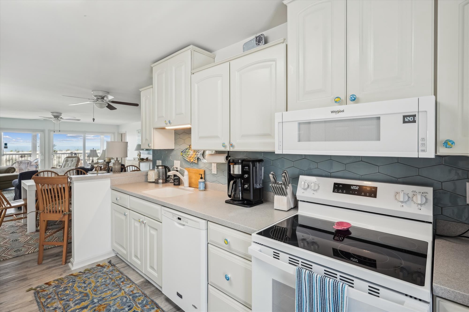 Your beach vacation kitchen awaits—bright white cabinetry, modern appliances, and seaside décor create the perfect spot to brew morning coffee while sunlight pours in from the coast.