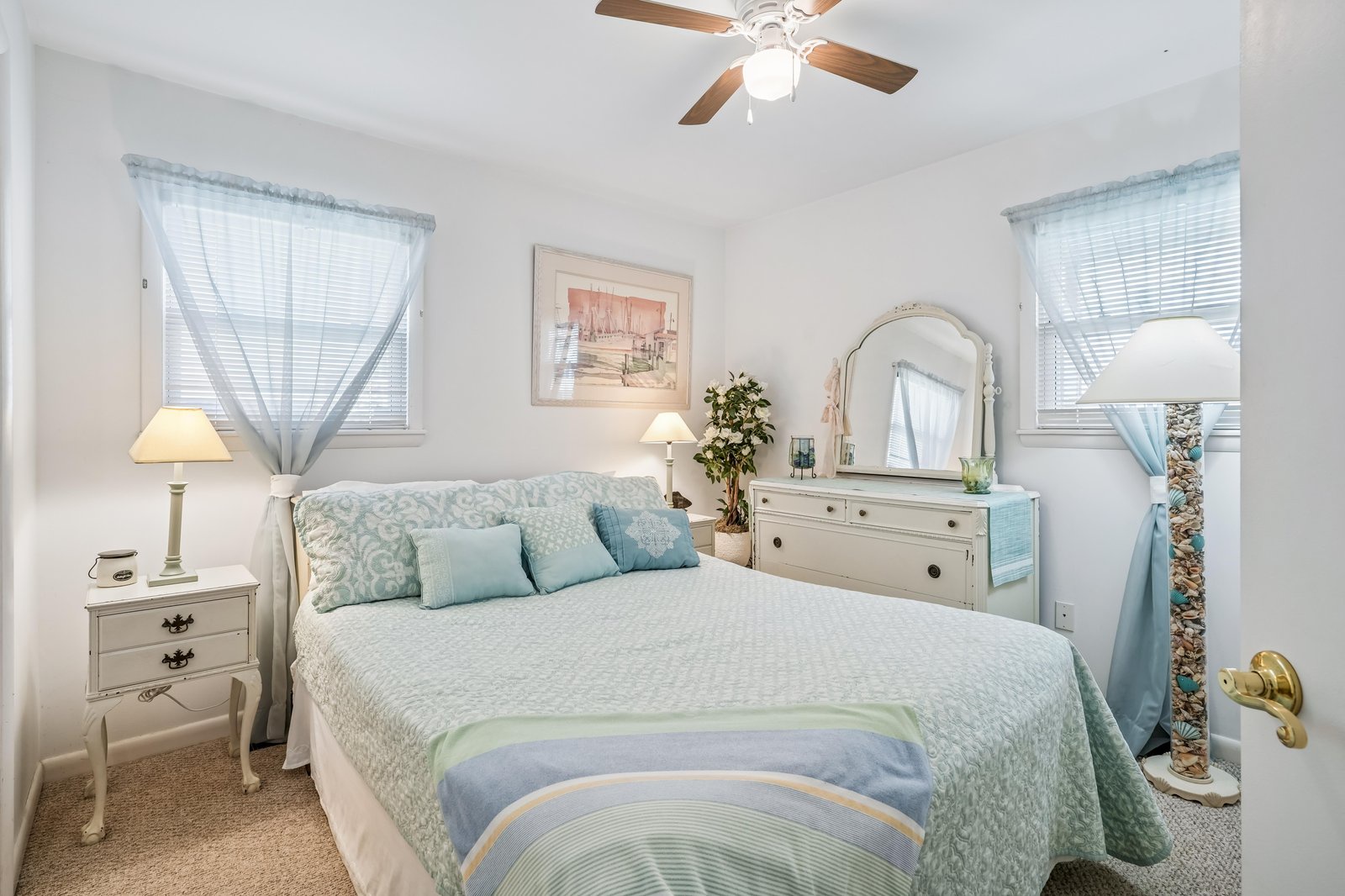 Relax in this tranquil bedroom with soft blue accents, crisp linens, and gentle natural light from two windows. The peaceful décor and cozy bedding invite restful nights.