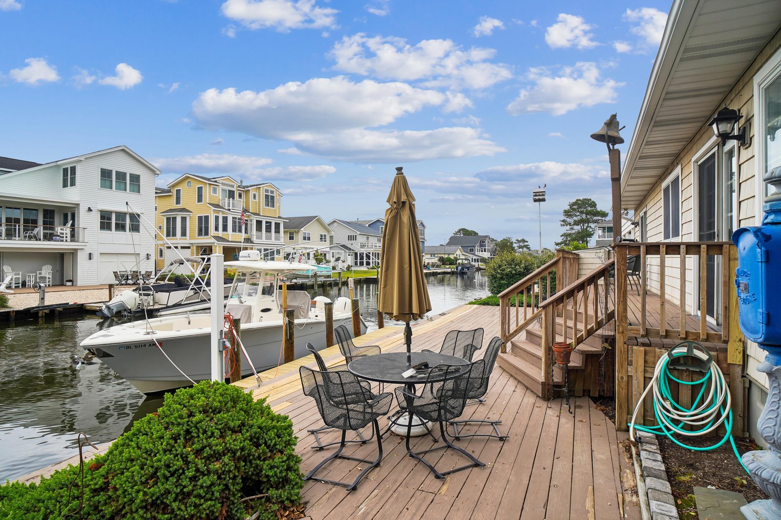 A charming waterfront deck with a private dock and boat slip, nestled in a peaceful residential canal community with colorful neighboring homes and open skies.