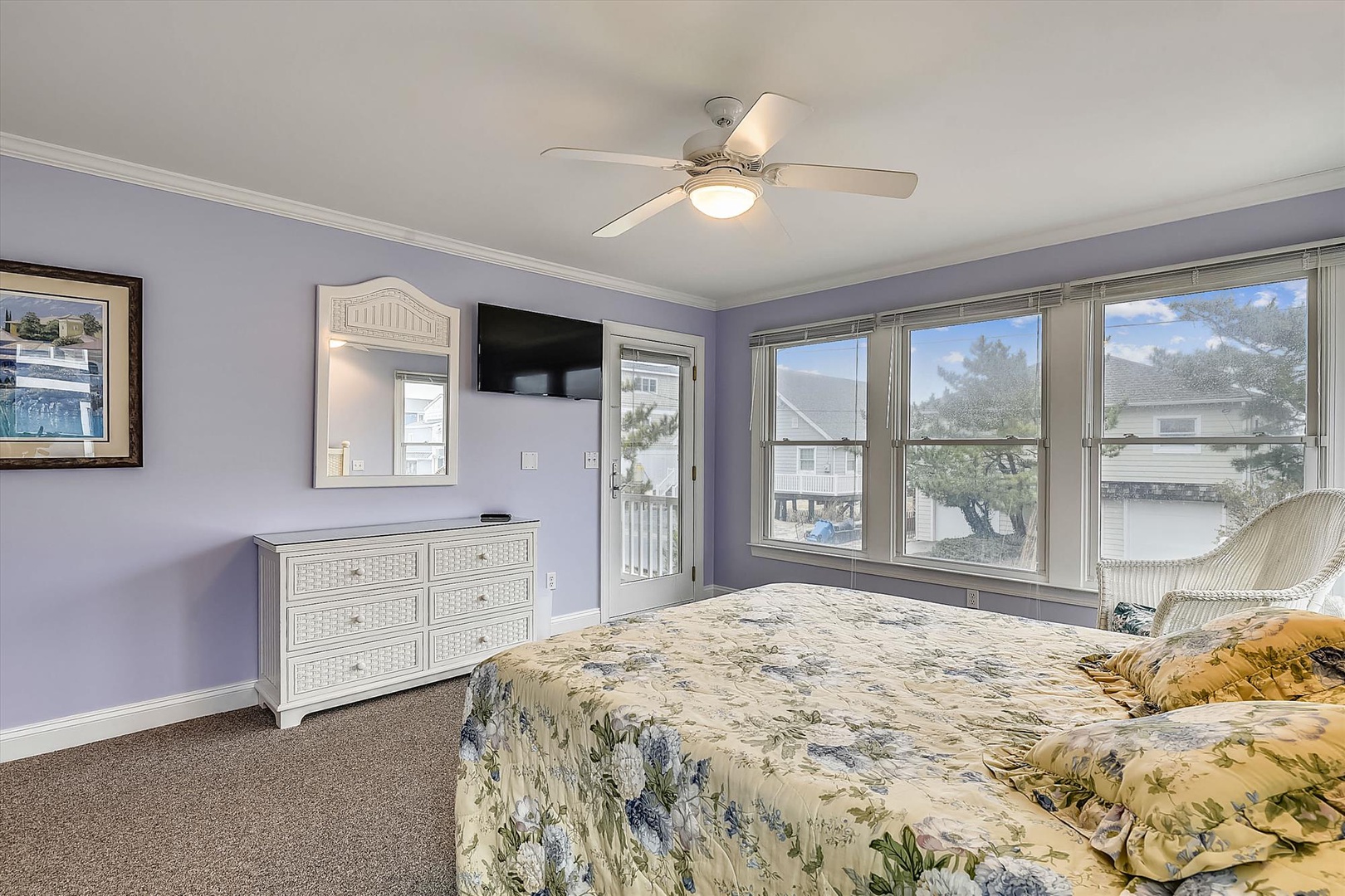 Your peaceful retreat features soothing lavender walls, a plush bed with floral linens, and large windows flooding the room with natural light—perfect for your restful mornings.