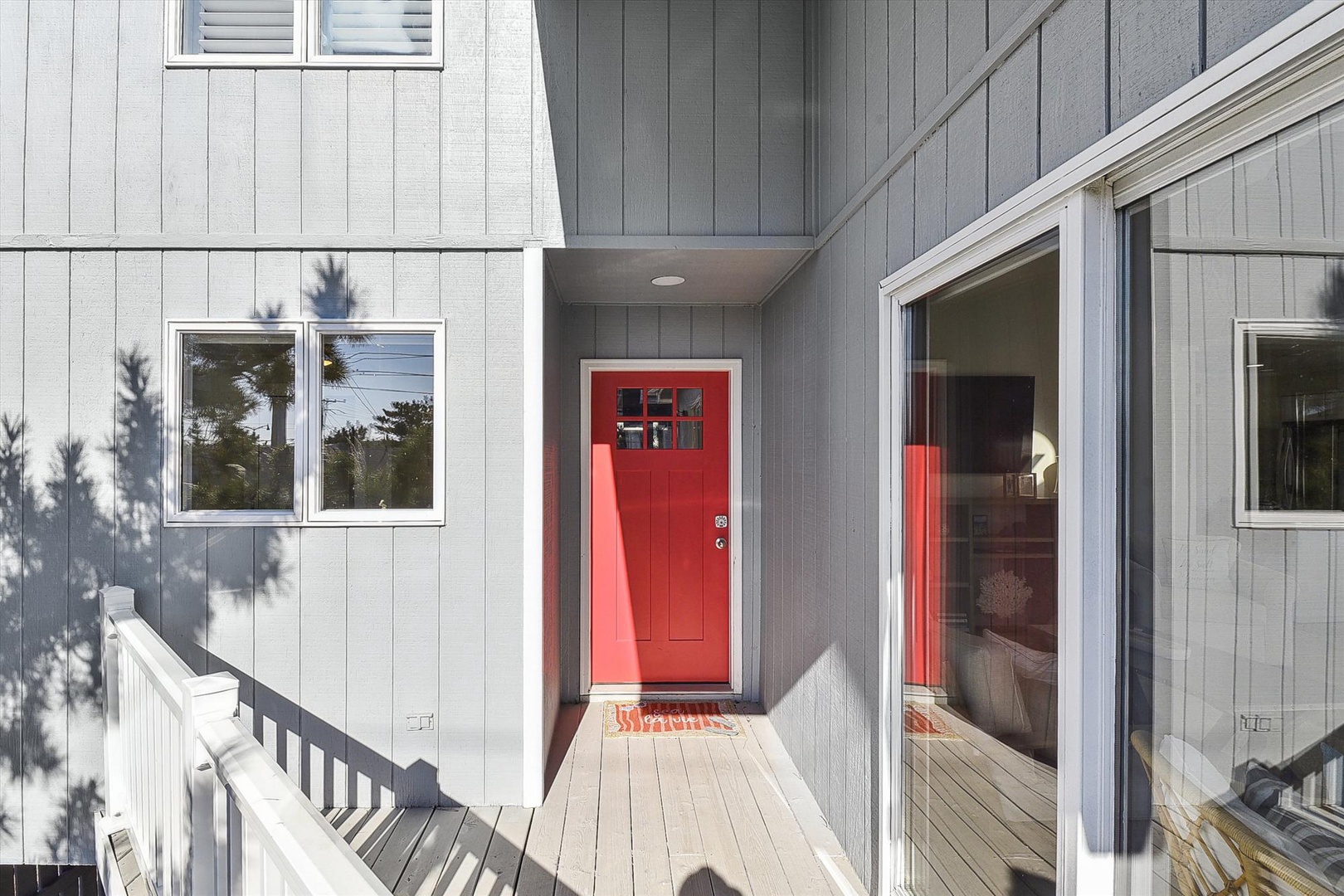 Modern coastal home featuring a bold red entrance door framed by light gray vertical siding, creating a welcoming arrival to your retreat.