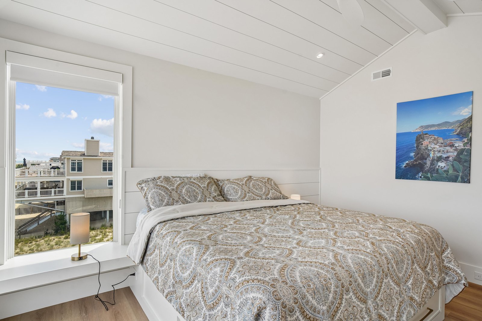 Unwind in this serene bedroom where crisp white walls meet vaulted shiplap ceilings. Your window frames neighborhood views, and the open layout invites peaceful rest after days of coastal adventures.