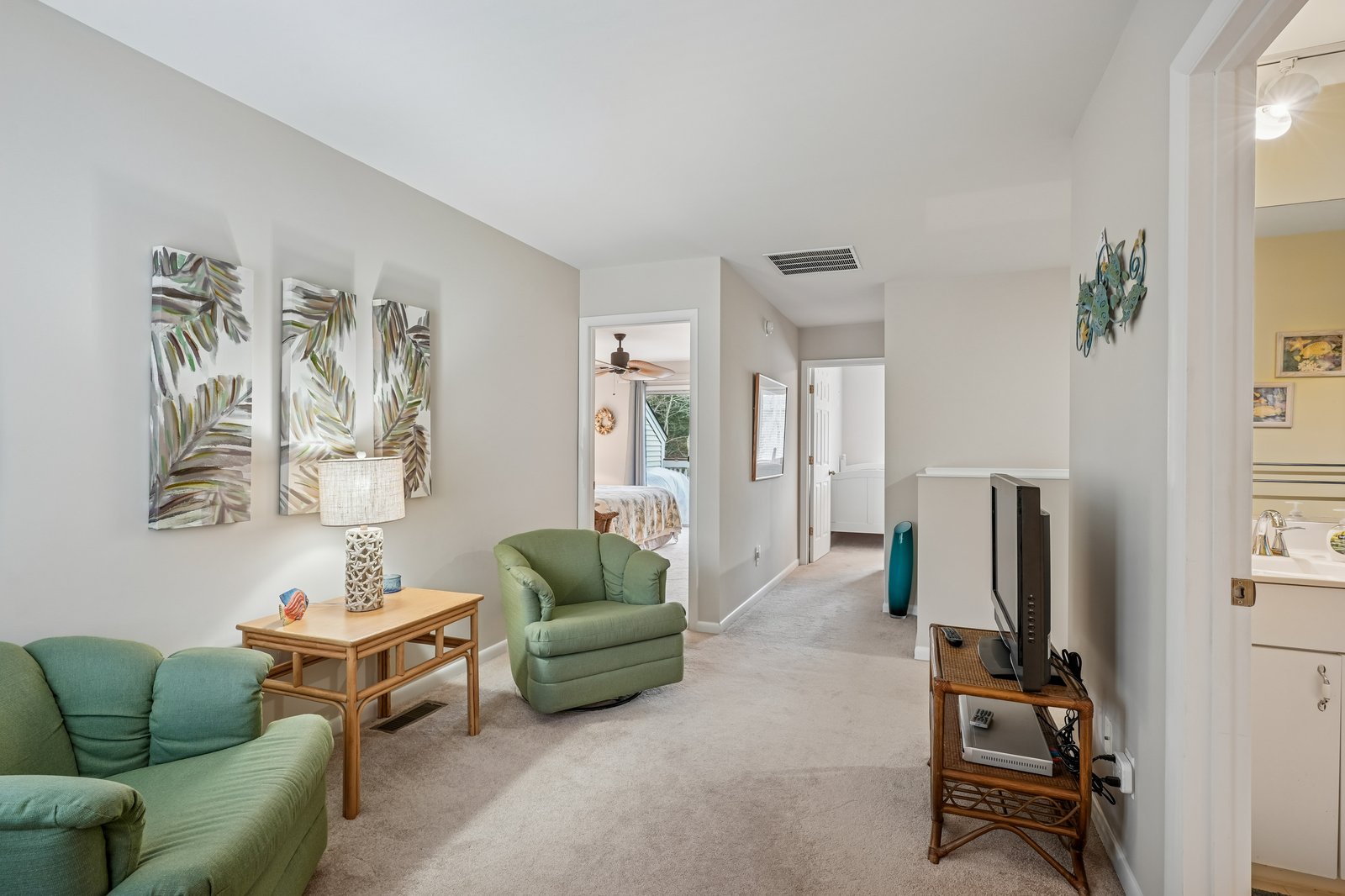 Relax in your bright living space featuring comfortable green seating, tropical artwork, and entertainment center for cozy evenings in.