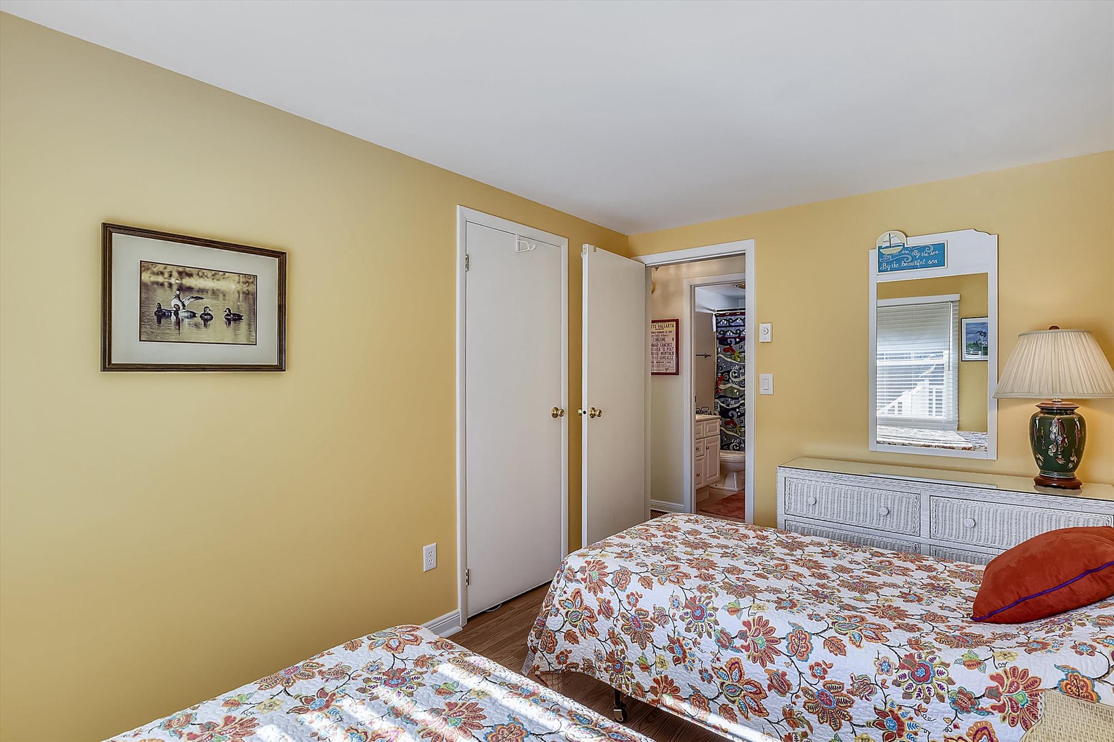 Your bright, welcoming retreat features two cozy beds dressed in charming patterned linens, warm yellow walls, and thoughtful touches like serene artwork and bedside lighting for restful nights.