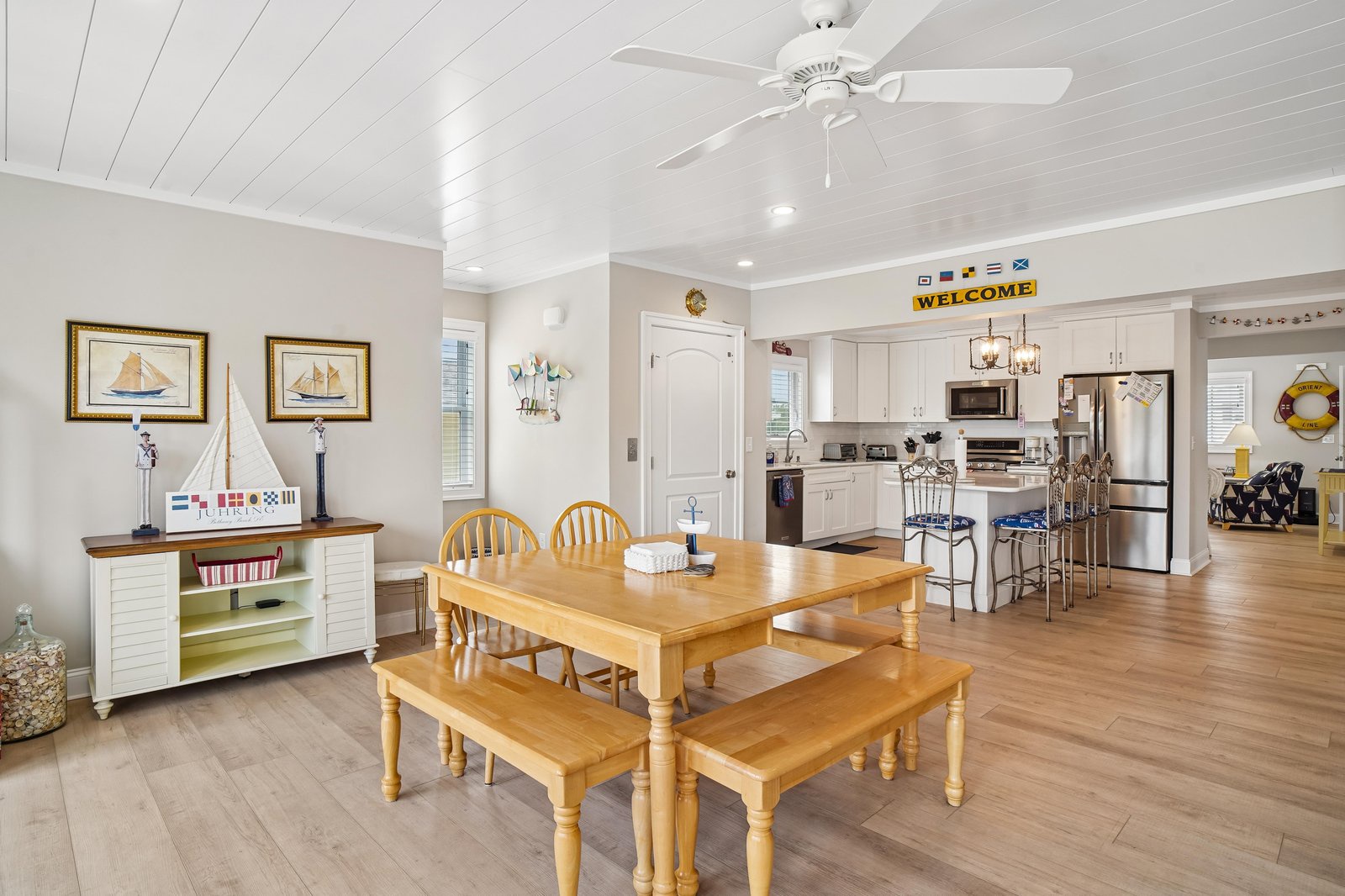 Step into this inviting open-concept space where coastal charm meets comfort. Gather around the solid wood dining table, whip up your favorite meals in the fully equipped kitchen, and feel the ocean breeze from the ceiling fan above.
