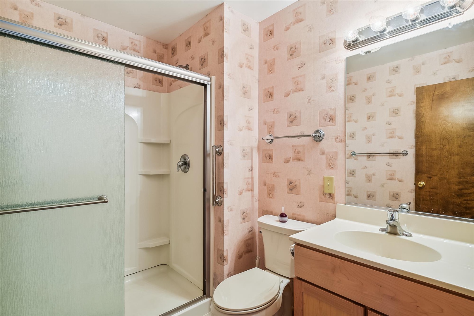 Your private bathroom features a spacious walk-in shower, vanity with ample counter space, and charming vintage wallpaper that adds cozy character.