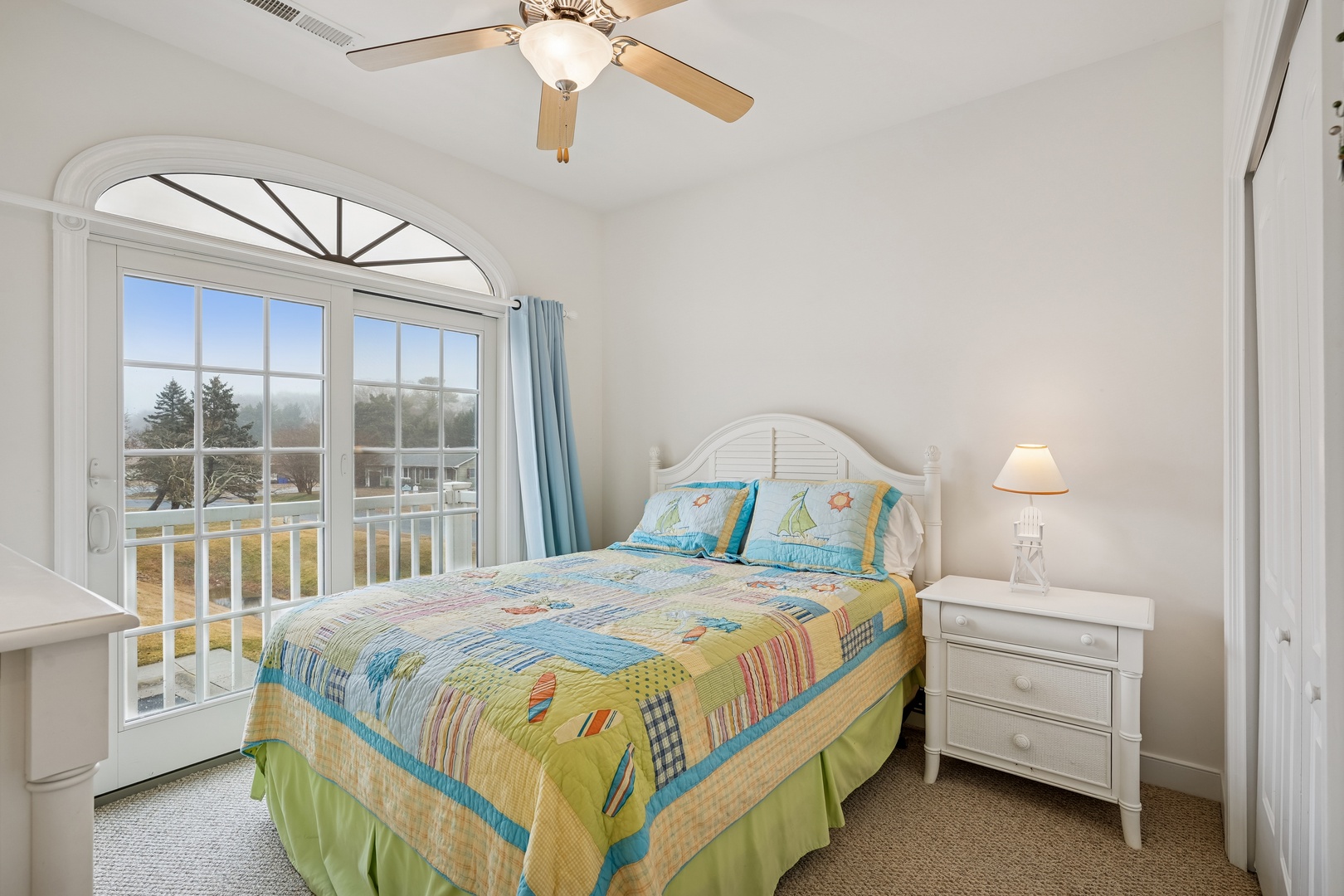 Step into your bright bedroom where cheerful coastal bedding and French doors create a perfect seaside retreat.