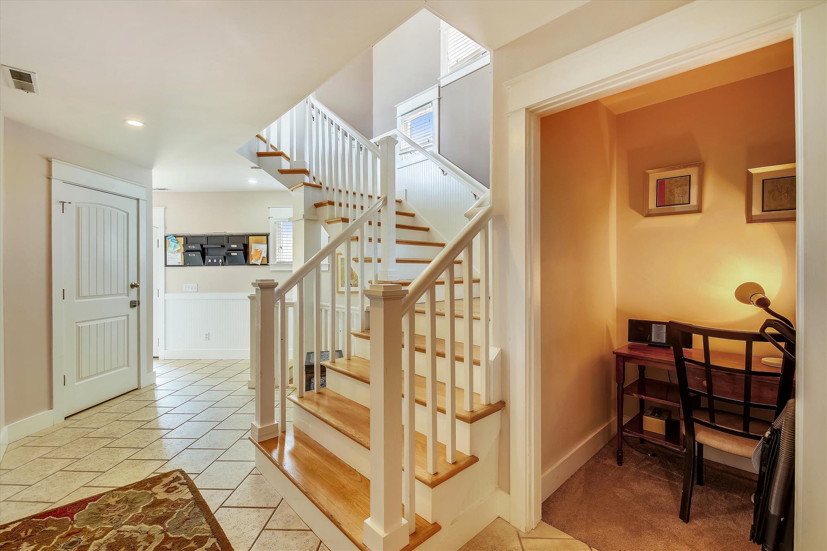 Bright and welcoming entryway with natural light flooding in, warm wood stairs guiding you upward, and a cozy workspace tucked to the side for your morning coffee or planning your day's adventure.