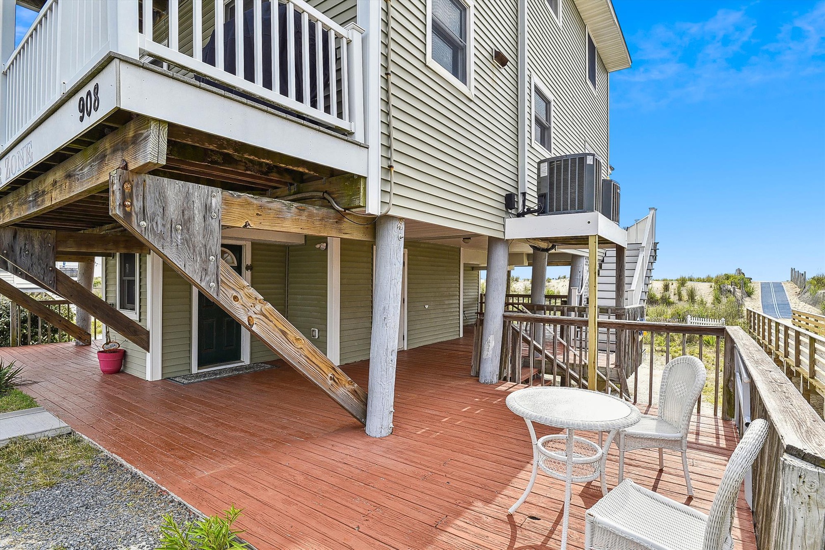 This elevated beach house sits on sturdy pilings with direct access to the dunes and shore. A spacious deck, numbered unit signage, and convenient outdoor seating create a welcoming coastal arrival experience.