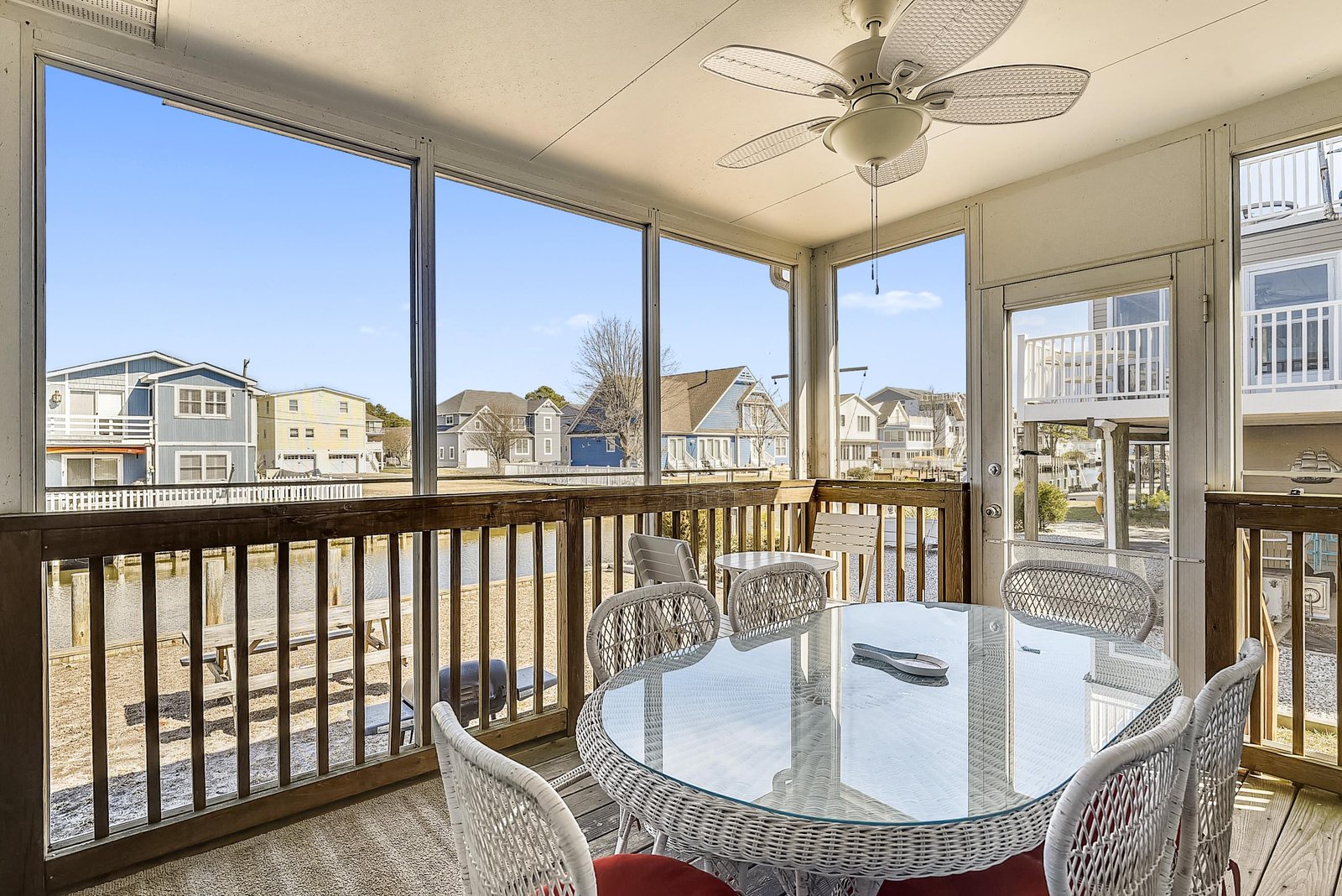 An enclosed porch offering neighborhood views through large windows. Gather around the dining table for meals or conversation while enjoying natural light and a gentle breeze from the ceiling fan.
