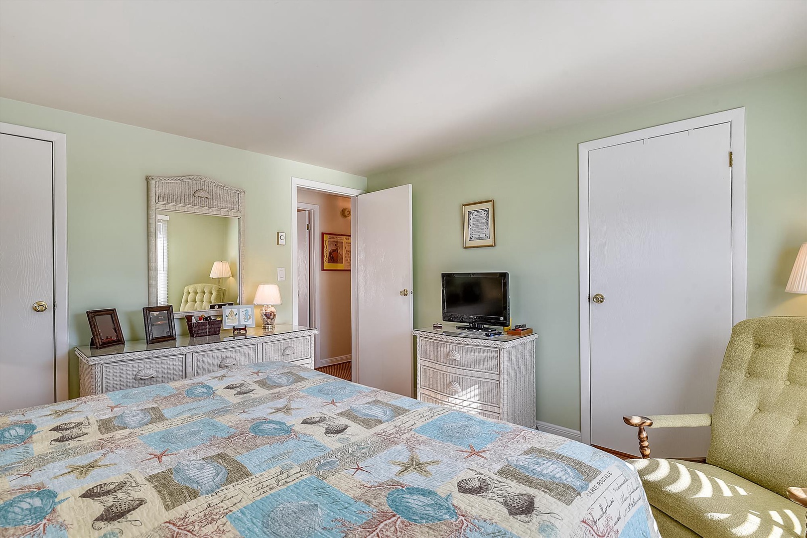 Unwind in your coastal-inspired bedroom featuring soft mint walls, wicker accents, and a charming seaside quilt that sets a relaxing, beachy tone for your stay.